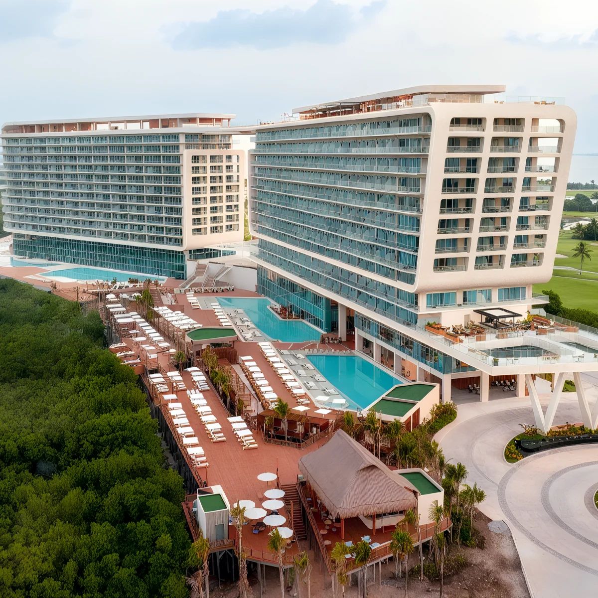 Aerial view of the Hyatt Vivid Grand Island, a modern beachfront resort featuring two tall buildings, a large swimming pool, sunbathing areas, and lush greenery.