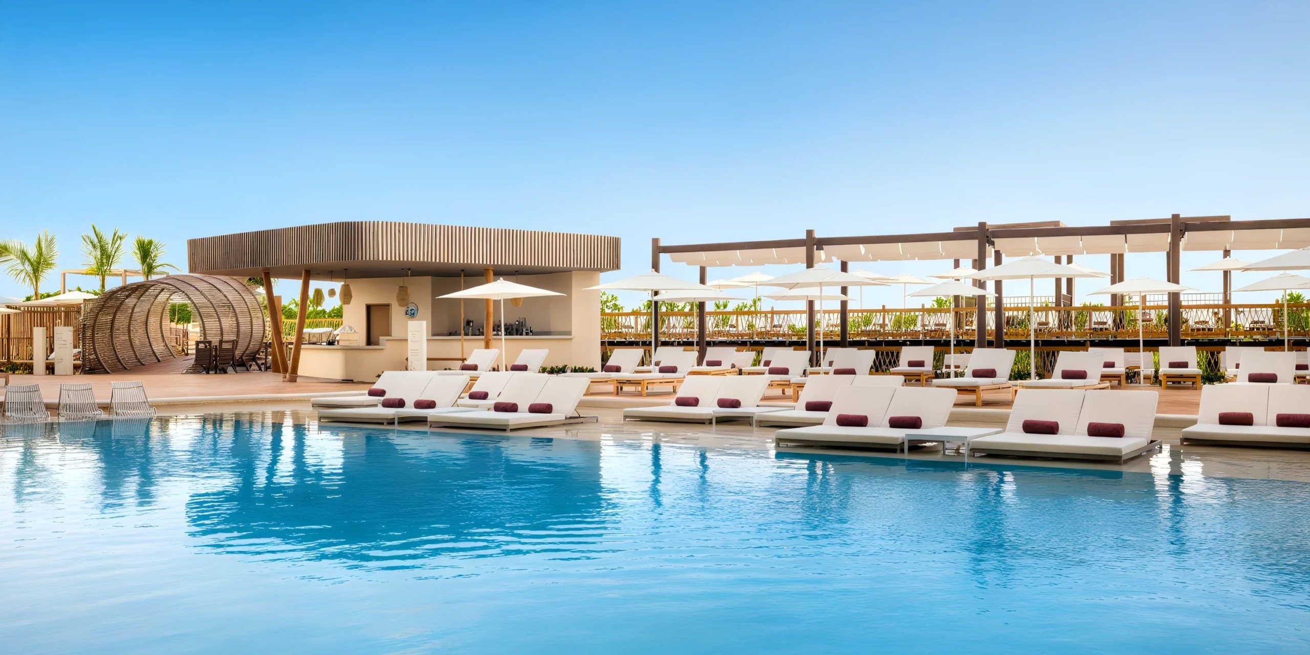 Hyatt Vivid Grand Island's outdoor pool area is complemented by white lounge chairs, umbrellas, and a modern cabana under a clear sky.