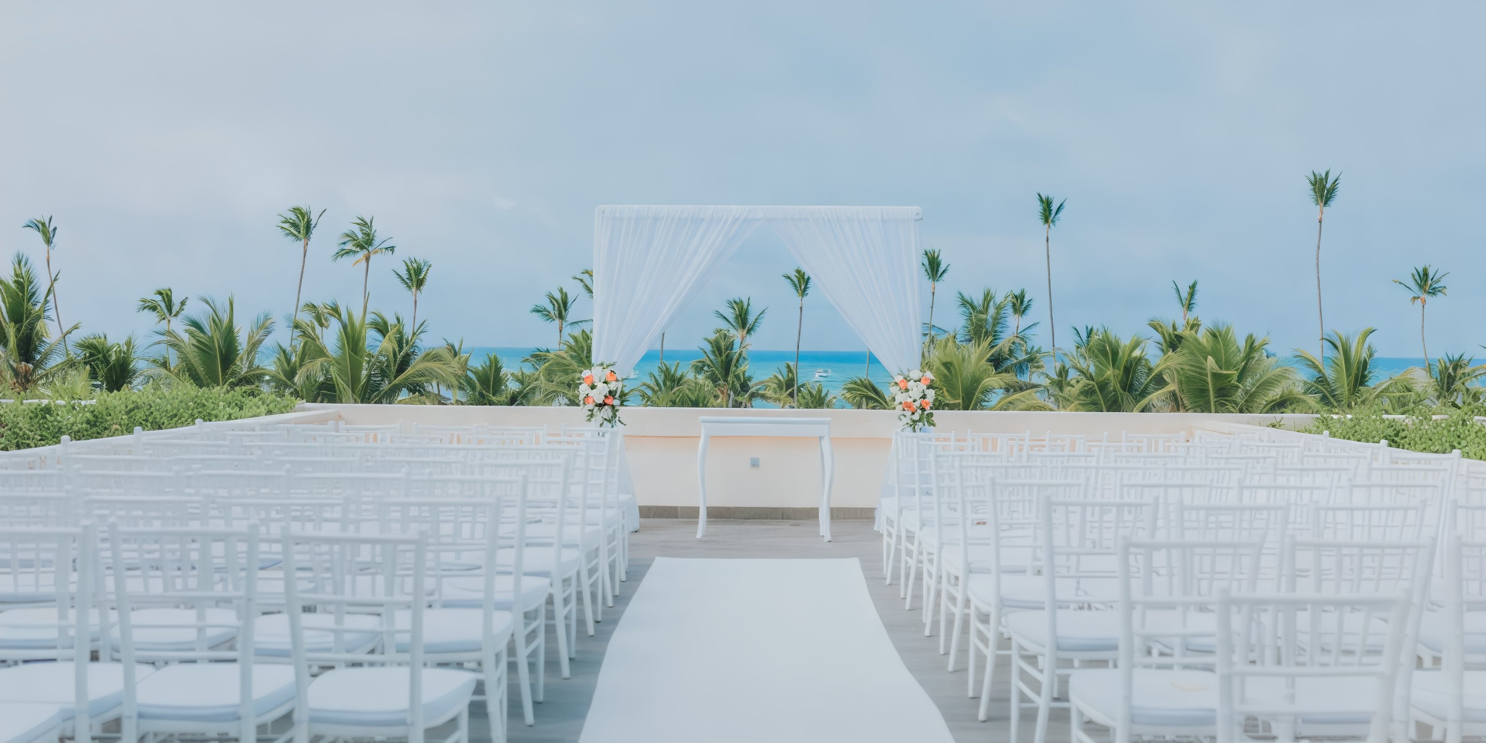 Experience a dream destination wedding at Lopesan Costa Bavaro, where white chairs are elegantly positioned around a picturesque arch, all set against the backdrop of a stunning tropical beach.
