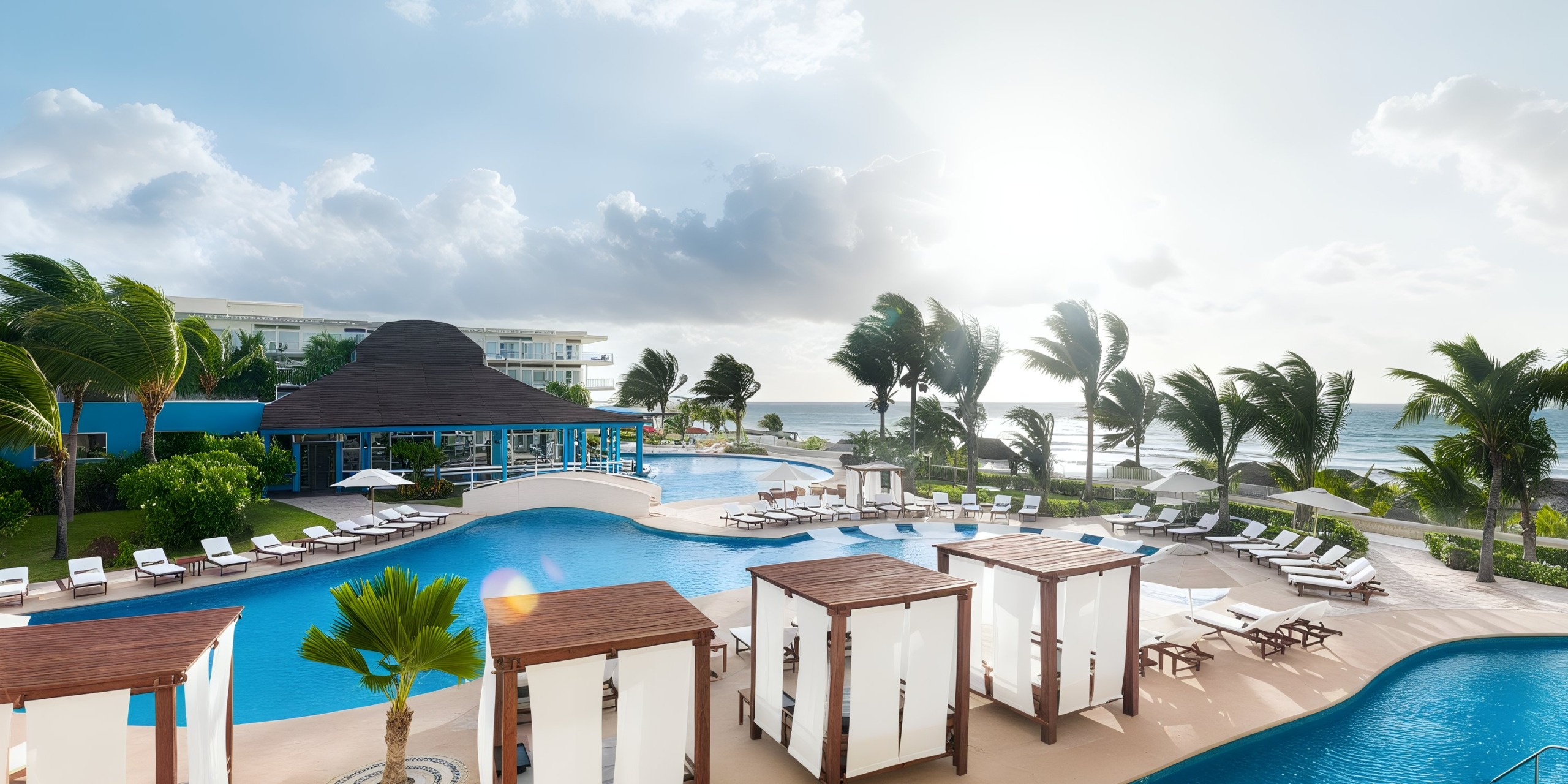 The Azul Beach Resort Riviera Cancun boasts a sprawling pool area complete with cabanas and lounge chairs, framed by palm trees and offering a beach view beneath a partly cloudy sky.