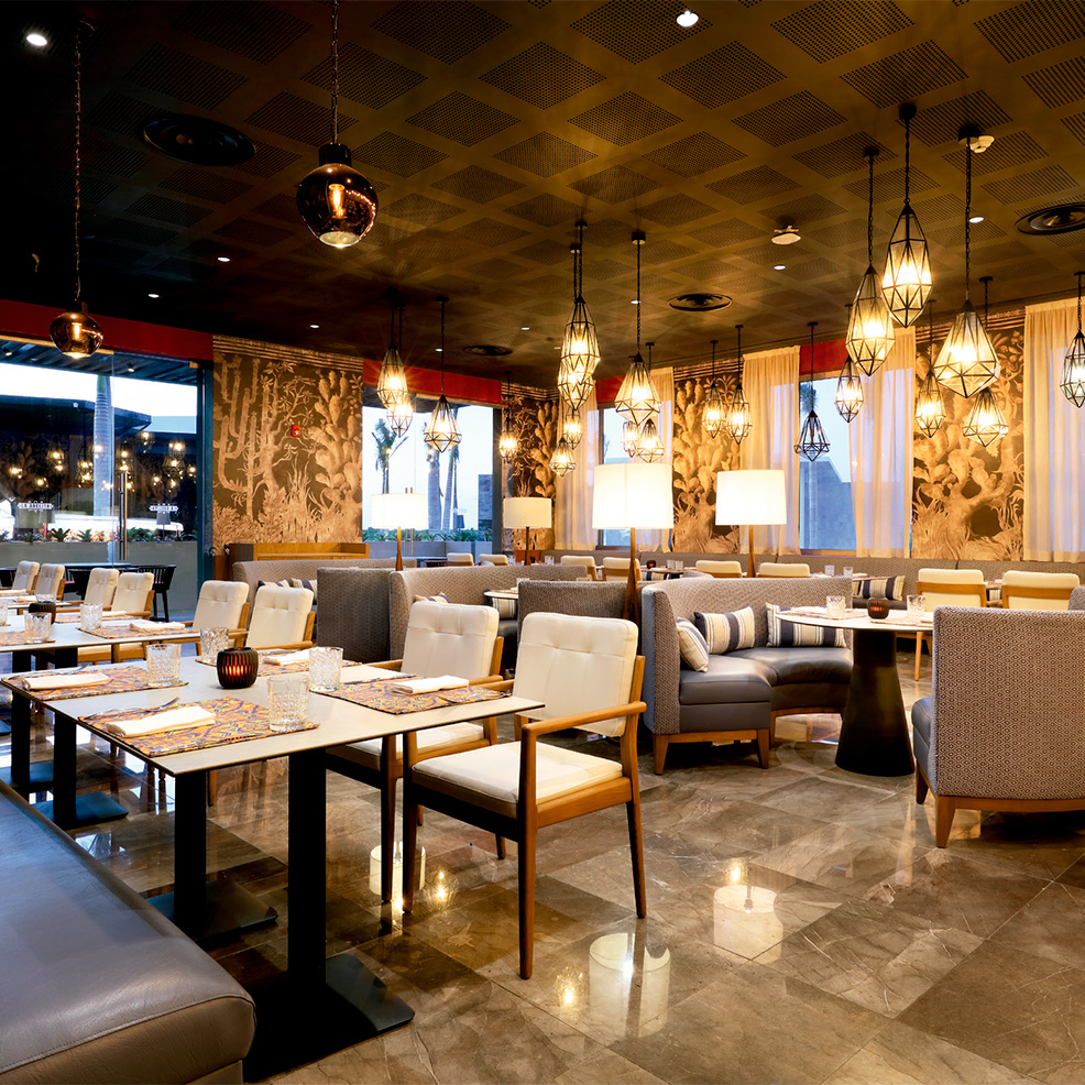 Elegant restaurant interior with modern lighting, cozy seating, and tables set with glasses and cutlery. Neutral tones and patterned walls enhance the ambiance.