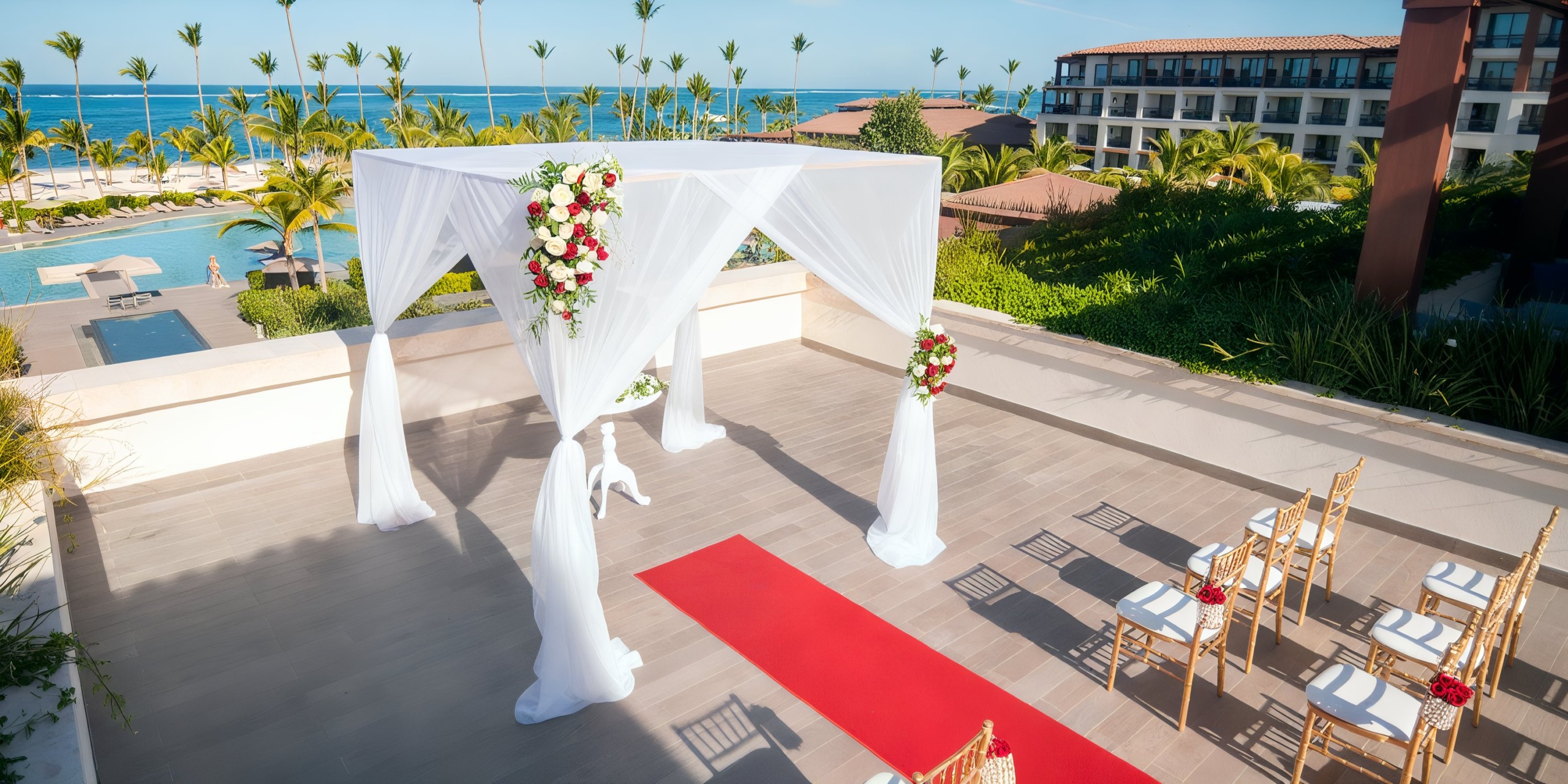 Experience a rooftop wedding setup at Lopesan Costa Bavaro, featuring a pristine white-draped canopy, stunning floral arrangements, a luxurious red carpet, and rows of chairs arranged to offer breathtaking views of the ocean.