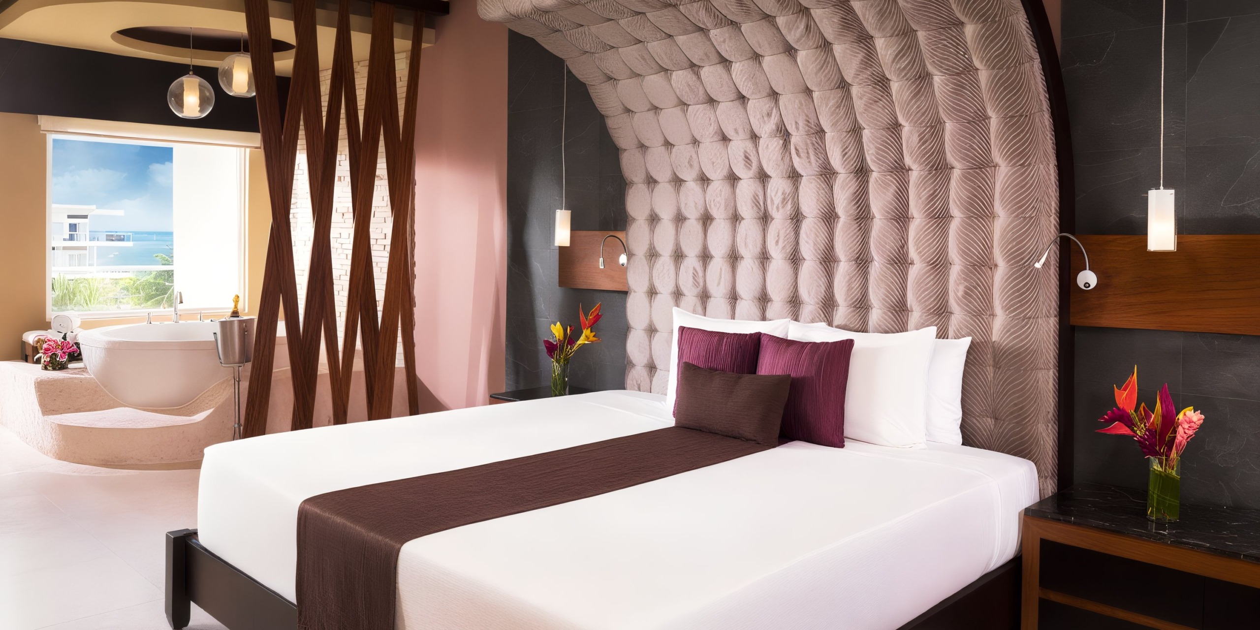 Experience a stay at Azul Beach Resort Riviera Cancun in a modern hotel room, complete with a large bed that boasts a padded, textured headboard. Enjoy the luxury of a freestanding bathtub positioned near the window, all amidst contemporary decor that features pendant lights and elegant floral arrangements.