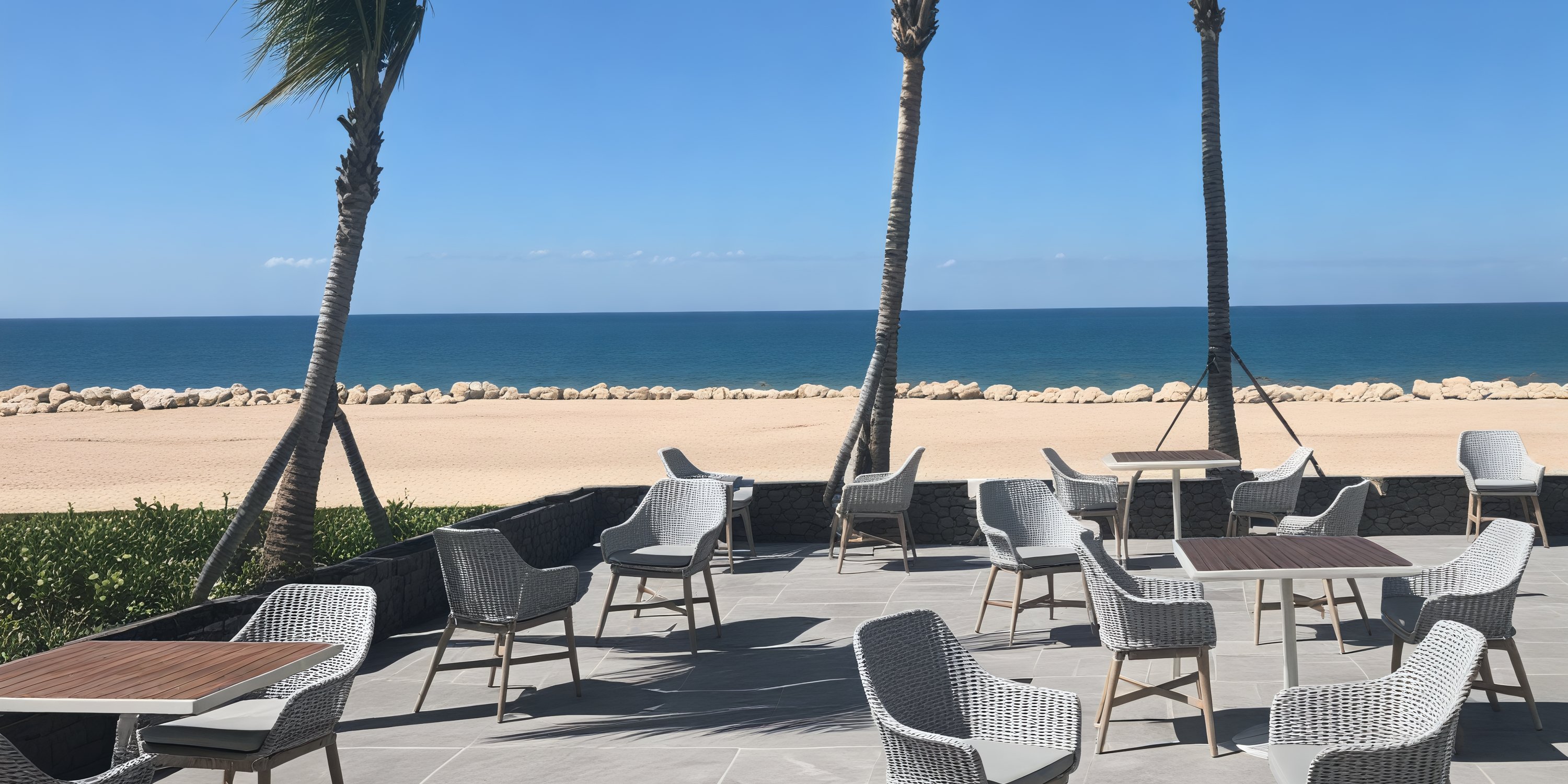 The patio at Princess Grand Jamaica overlooks a sandy beach and the ocean under a clear sky, providing an idyllic setting for a destination wedding.