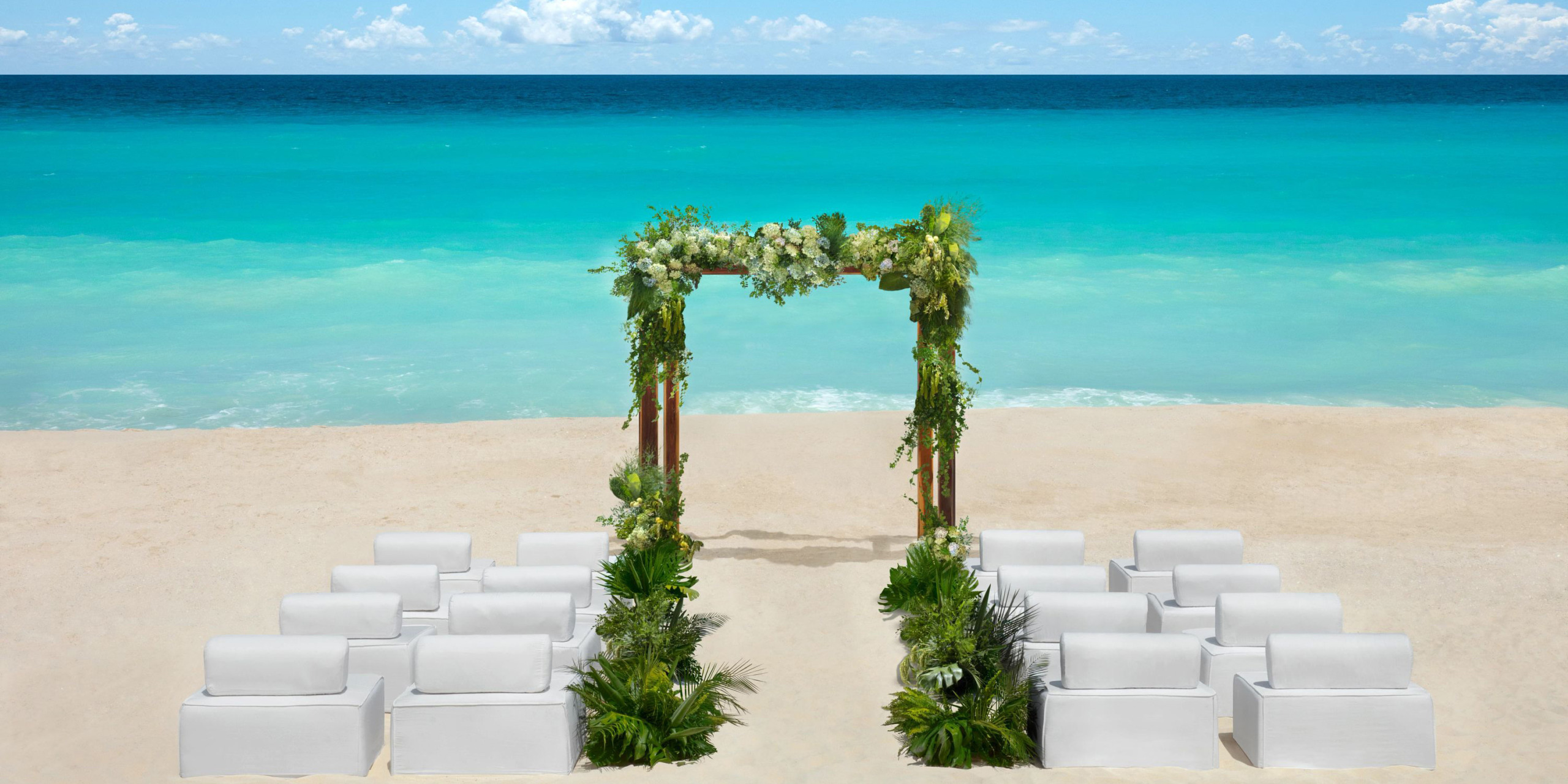 Hyatt Vivid Grand Island offers a beach wedding setup featuring a floral arch facing the ocean and surrounded by white chairs elegantly placed on the sand.