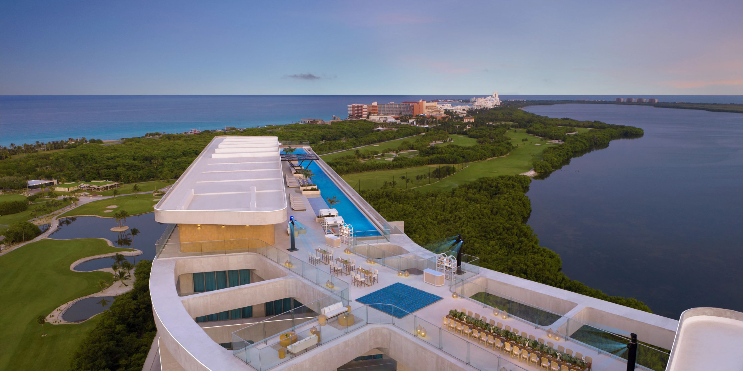 The Hyatt Vivid Grand Island offers a rooftop terrace with a pool that provides stunning views of a golf course, lush greenery, and the ocean beneath a clear sky.