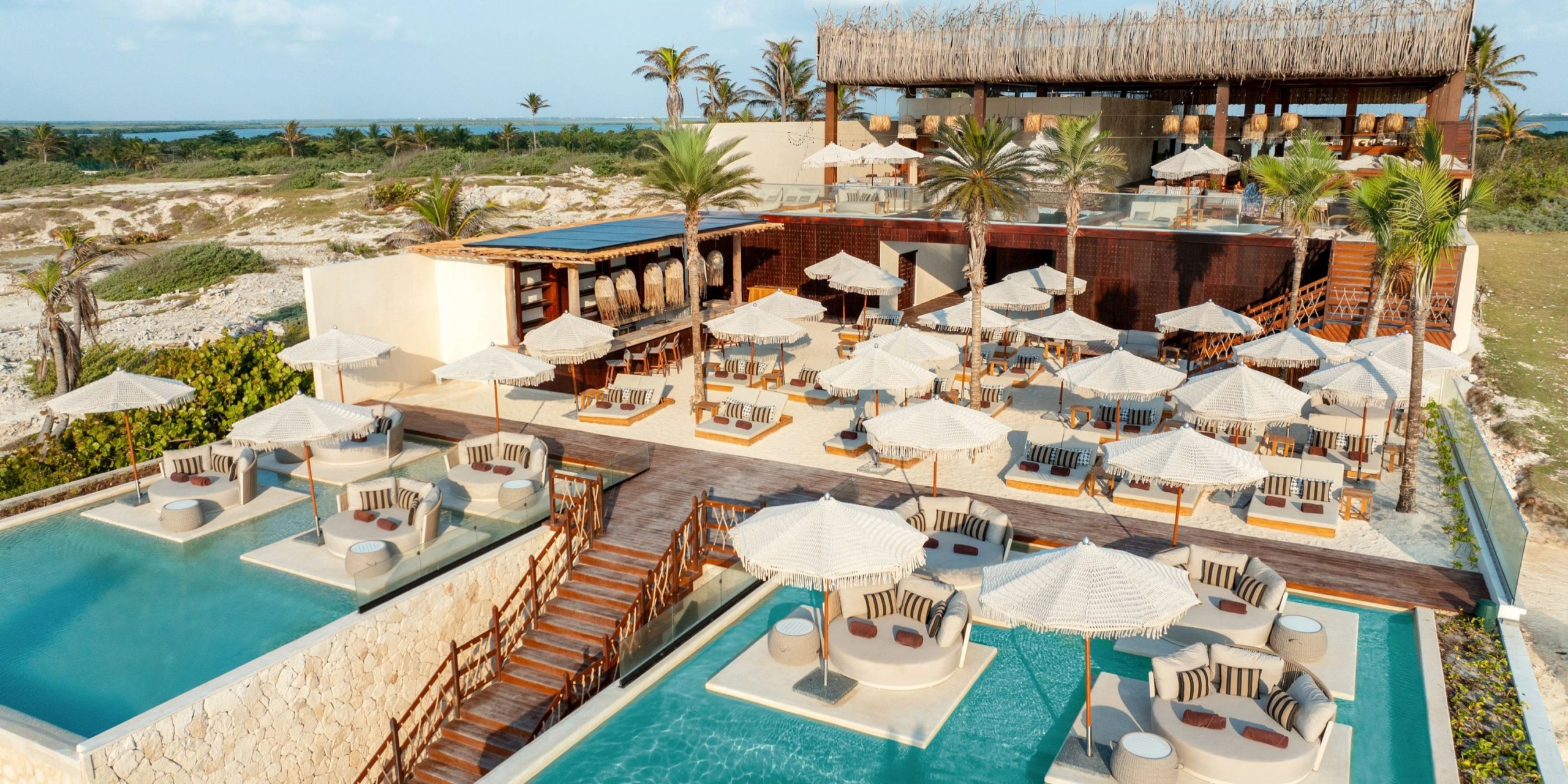 Aerial view of the Hyatt Vivid Grand Island showing an outdoor resort area featuring lounge chairs, umbrellas, and two adjacent swimming pools surrounded by palm trees.