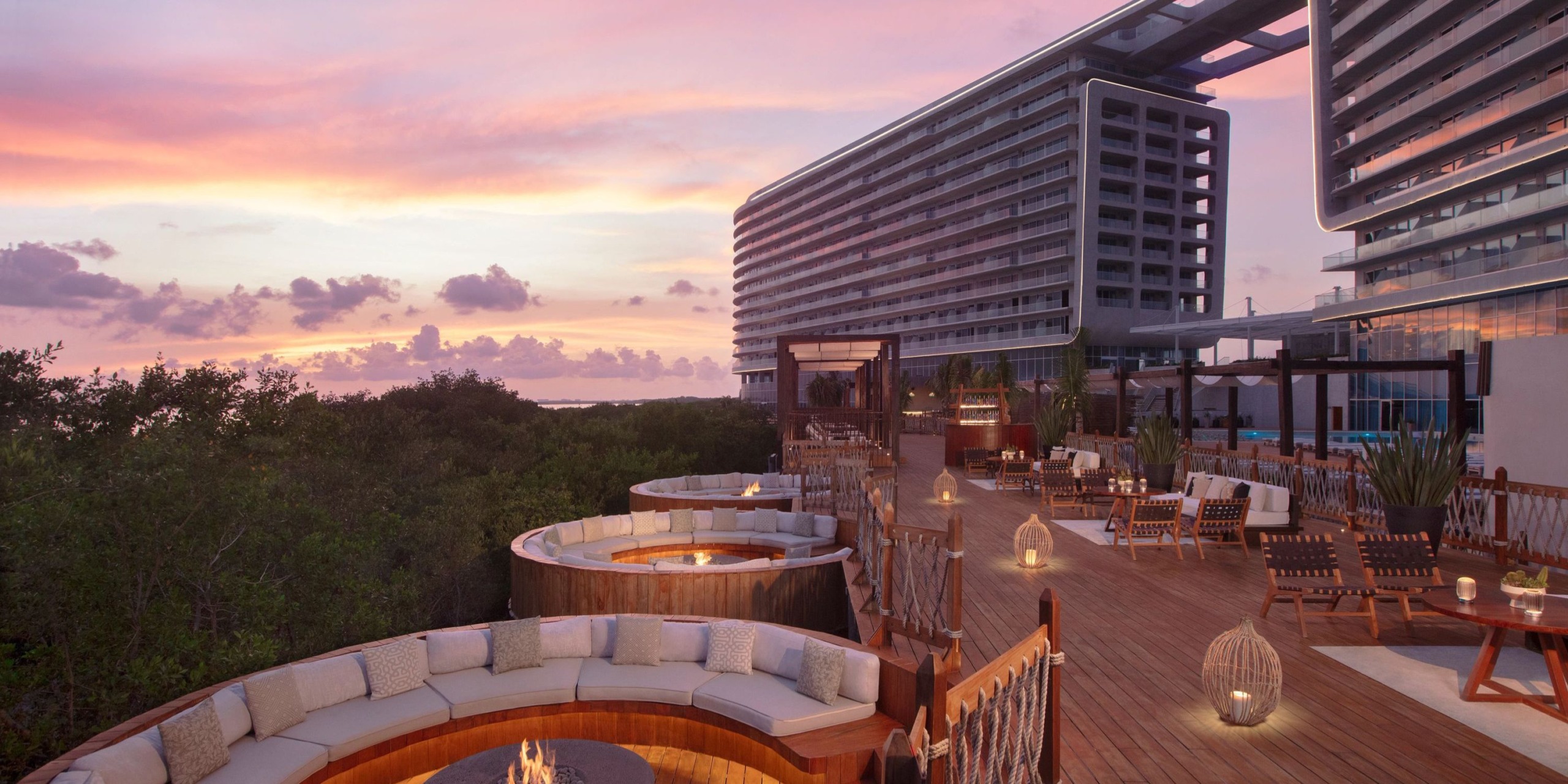 Experience the Hyatt Vivid Grand Island's outdoor terrace at sunset, featuring circular seating around fire pits and surrounded by modern architecture and lush greenery.