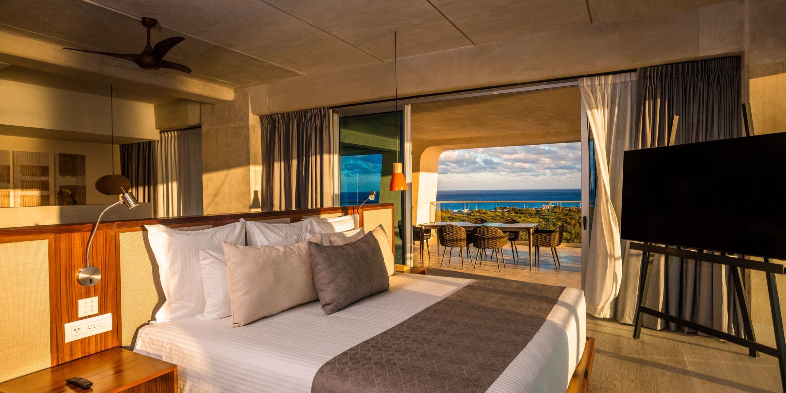 Experience the Hyatt Vivid Grand Island, featuring a contemporary room with a spacious bed, elegant neutral decor, and a wall-mounted television. Sliding glass doors reveal a balcony complete with seating and stunning ocean views.