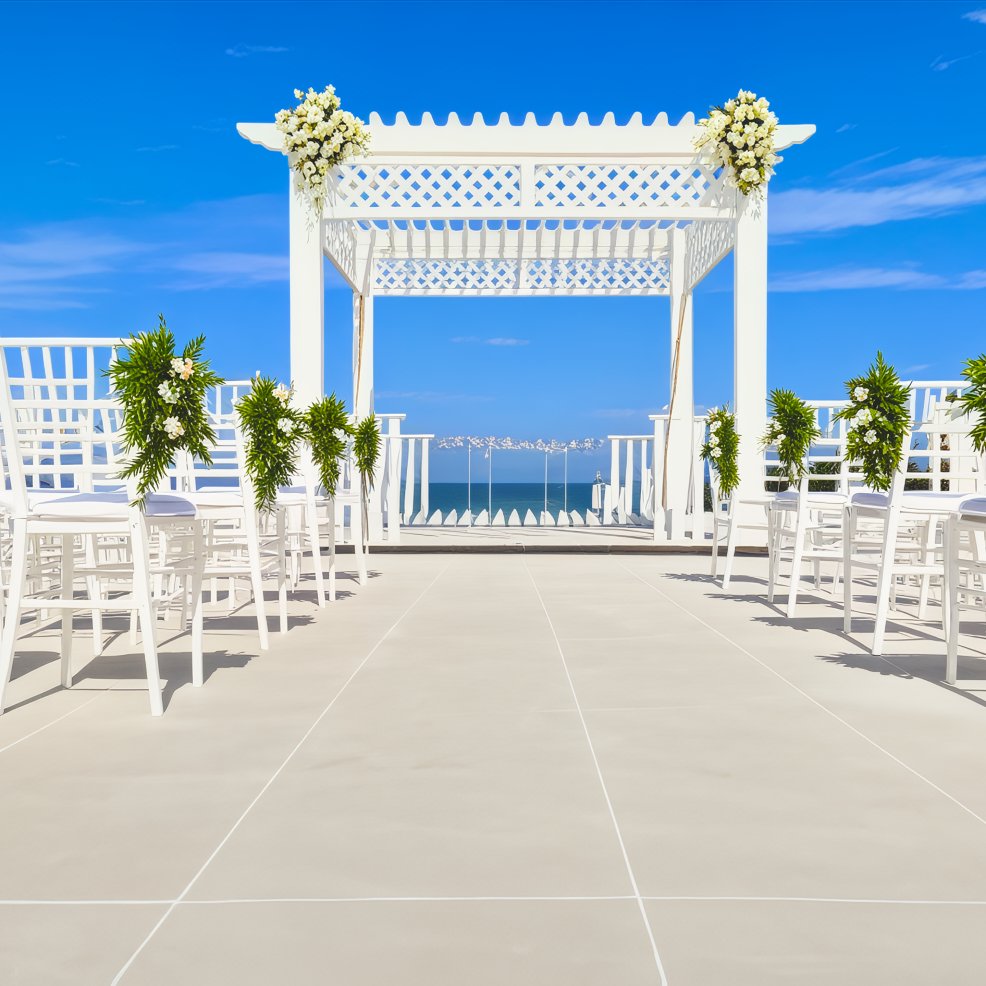 An elegant white gazebo set up for a wedding ceremony is arranged with chairs that offer breathtaking views of the ocean, creating the perfect setting for a picturesque destination wedding.