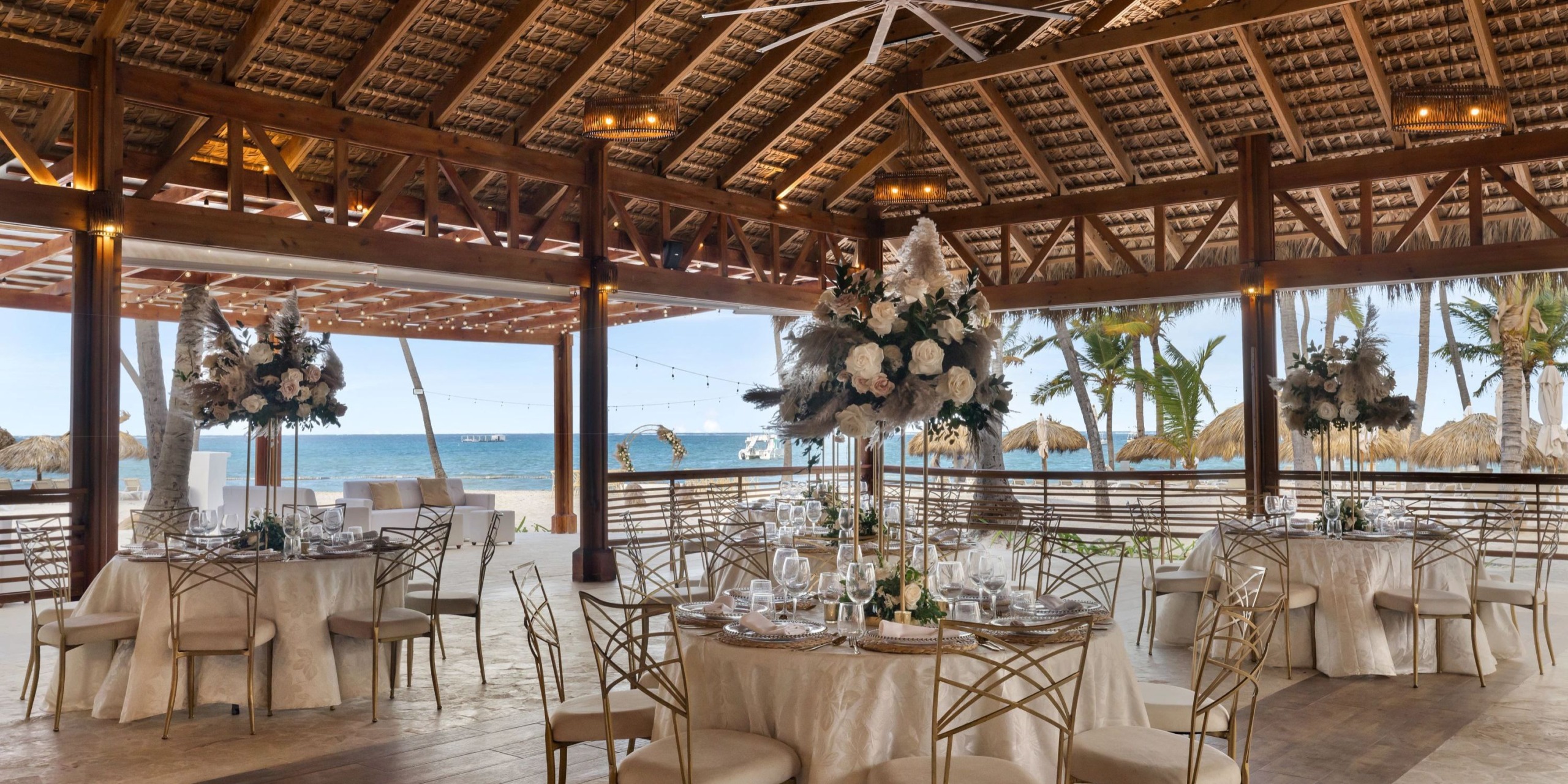 Beachside wedding reception setup at Sunscape Dominicus La Romana under a wooden pavilion with decorated tables and an ocean view in the background.