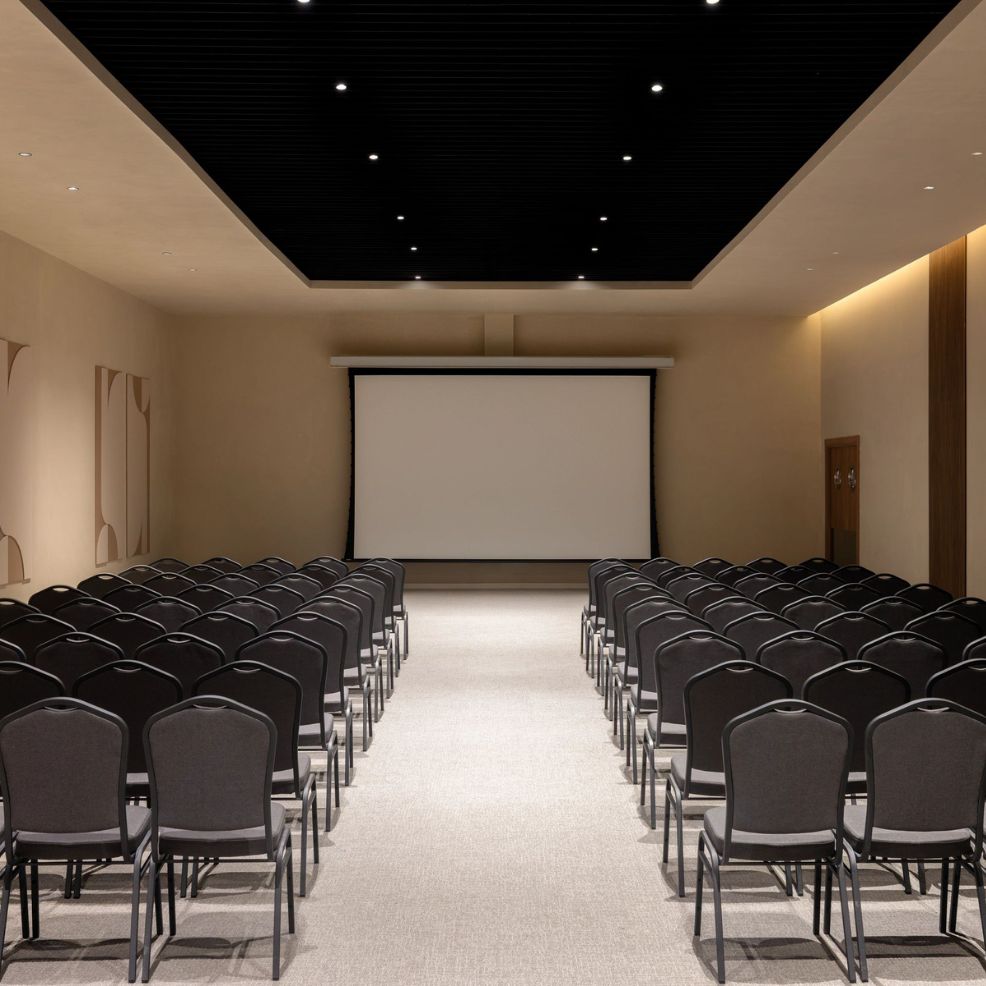 Empty chairs face a large screen in the Secrets Baby Beach Aruba conference room set for a destination wedding.