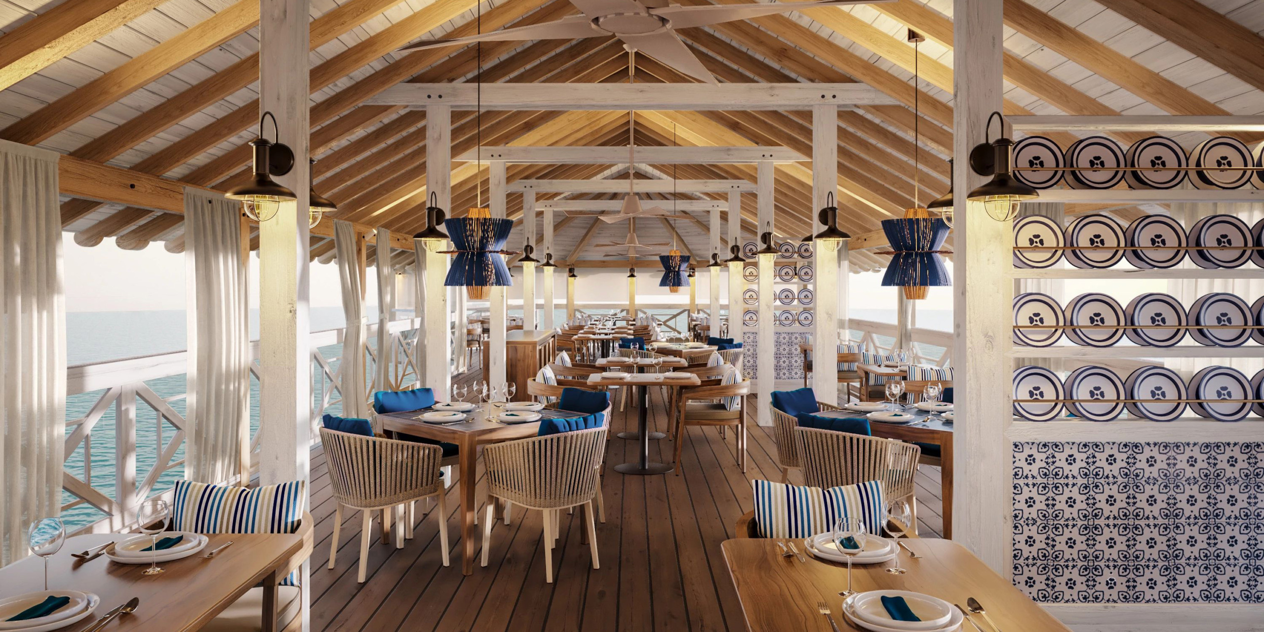 The interior of Secrets St Lucia features a coastal design with wooden tables and chairs, blue and white decor, and ceiling fans. Expansive windows provide stunning views of the sea.