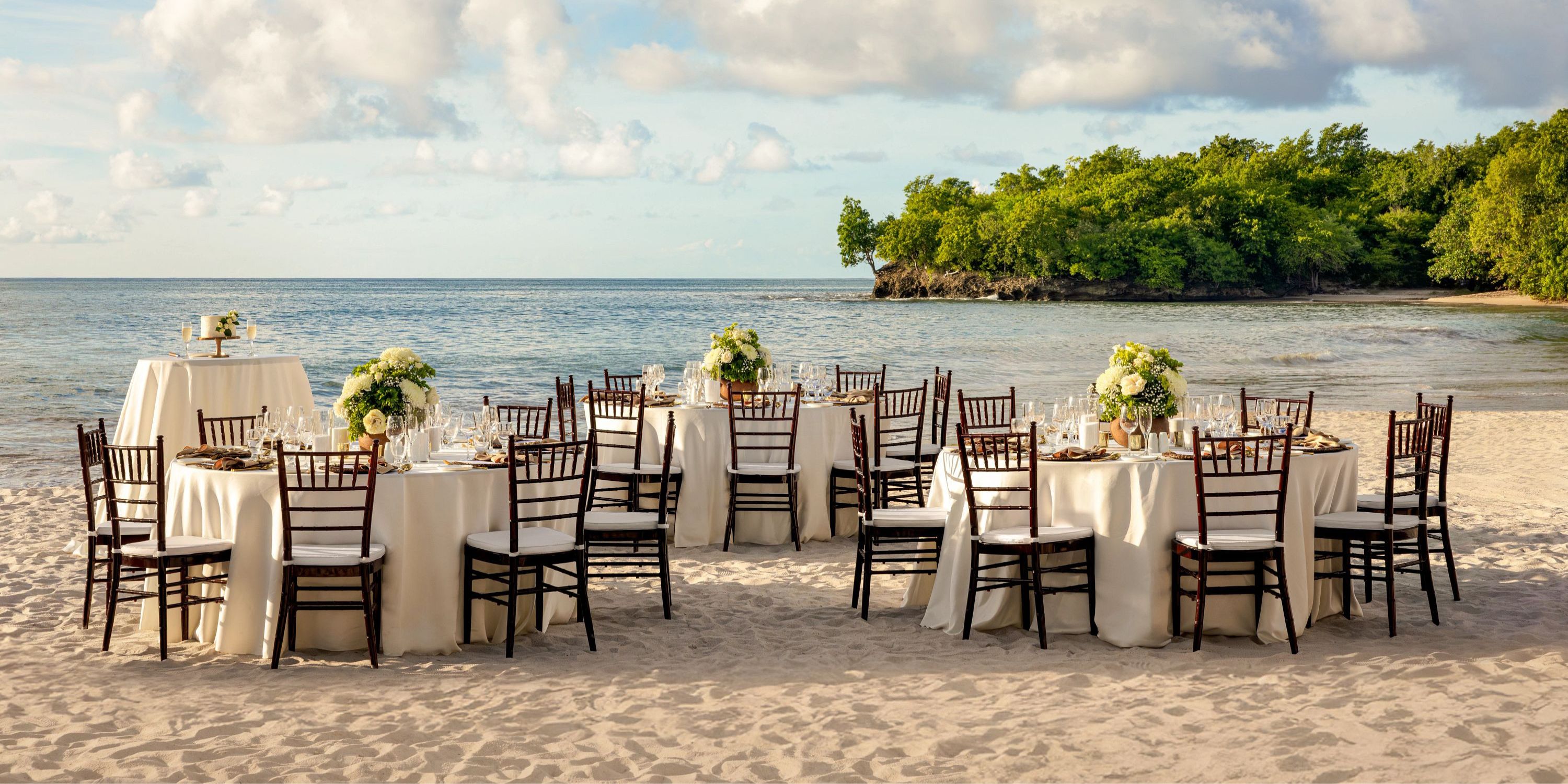 Secrets St Lucia: round tables with white cloths and chairs on a sandy beach, perfect for a destination wedding.