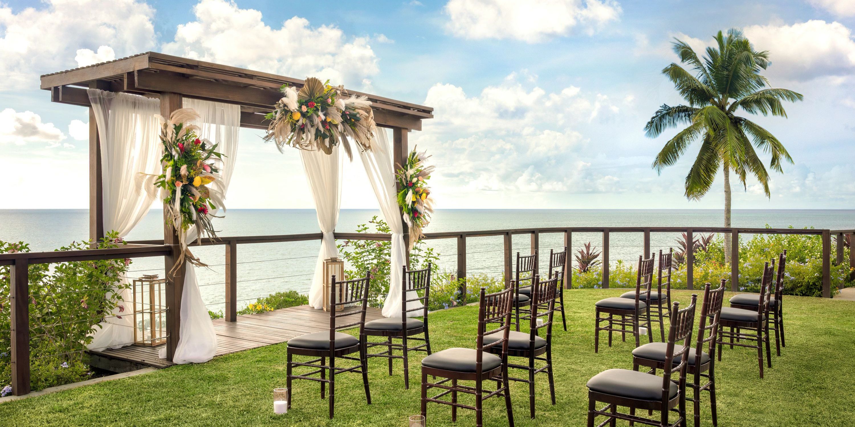 Secrets St Lucia: Destination wedding setup with chairs and arbor overlooking the ocean beneath clouds.