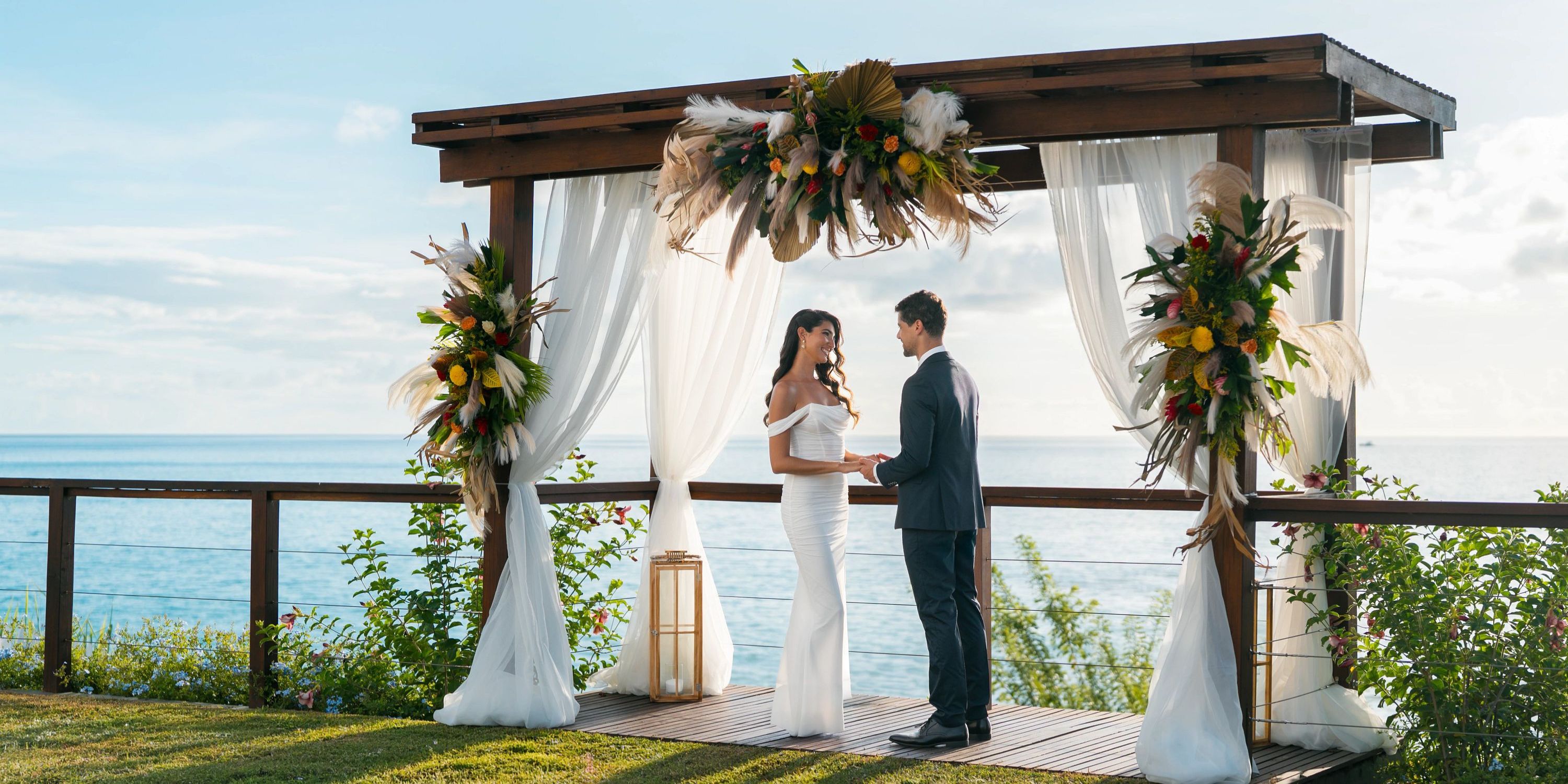 A couple holds hands under a wedding arch by the ocean during their destination wedding at Secrets St Lucia.