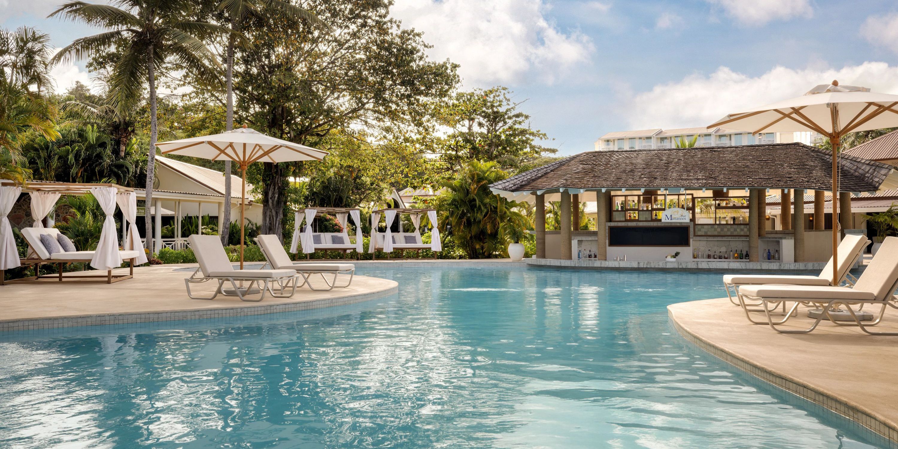 Secrets St Lucia: Ideal destination wedding setting with pool, loungers, umbrellas, bar, and tropical greenery.
