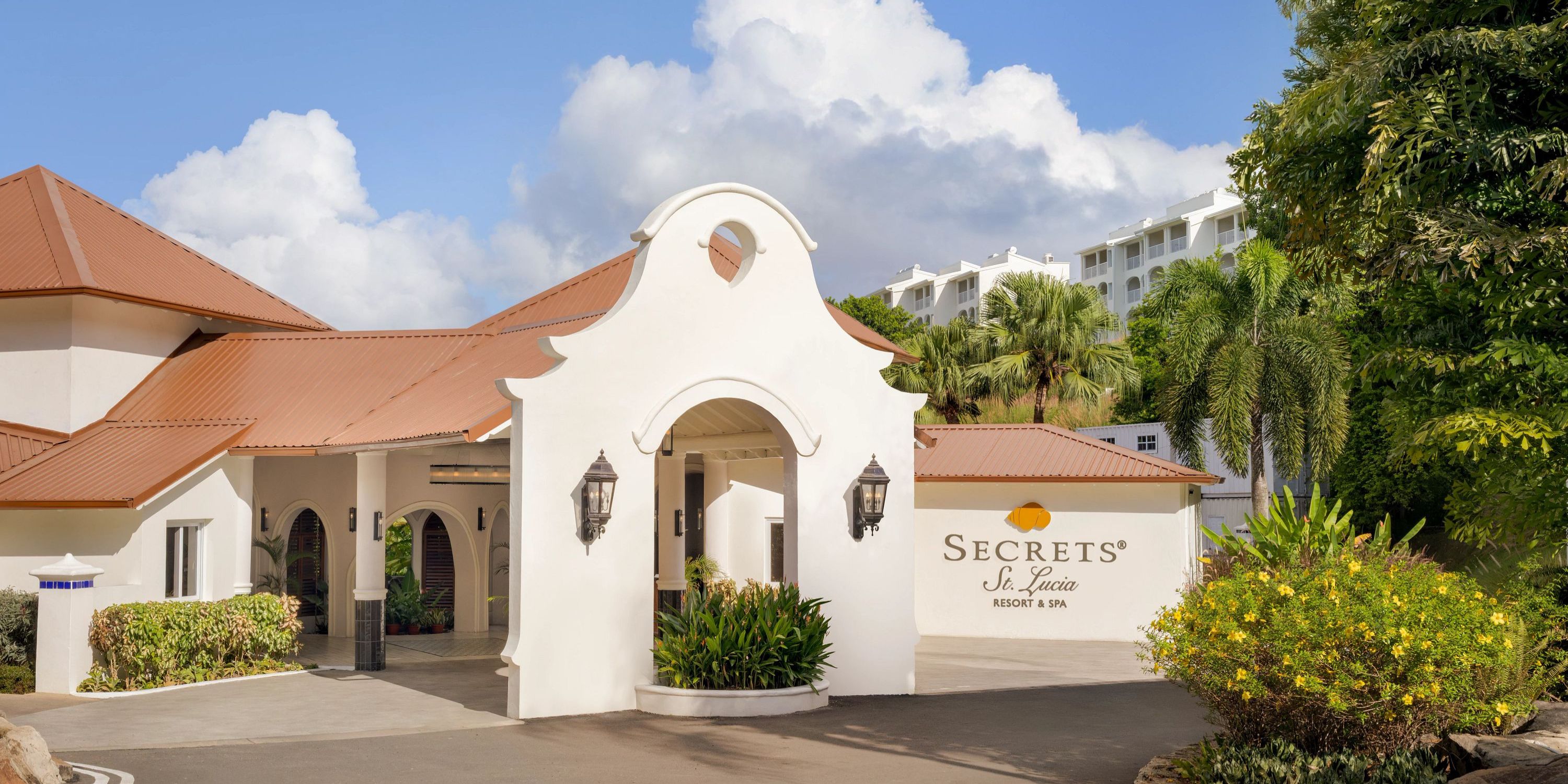 White stucco entrance of Secrets St Lucia, perfect for a destination wedding, with red roof and palms.