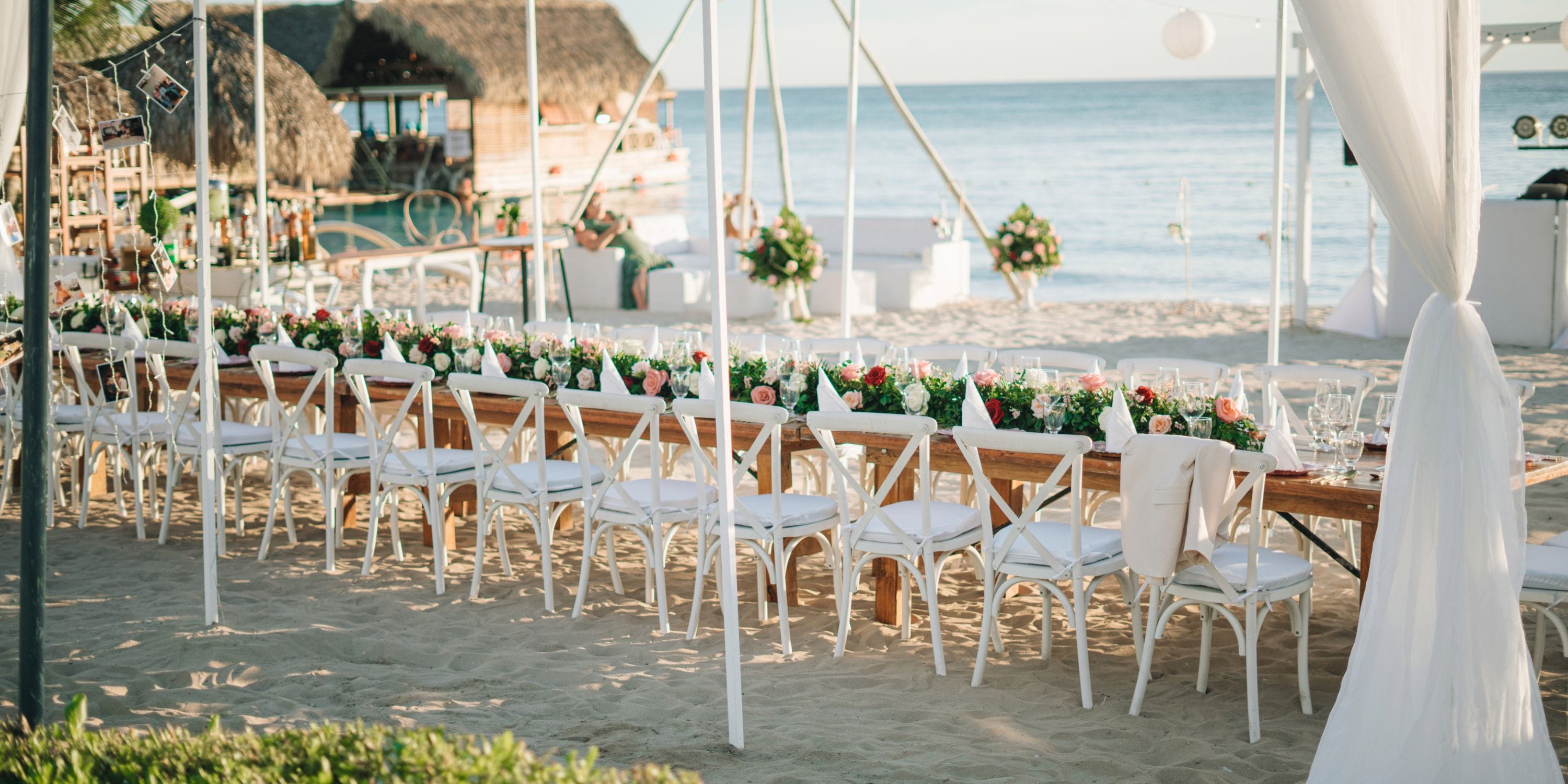 Long table with white chairs arranged for a destination wedding on the sandy beach at Sunscape Dominicus.