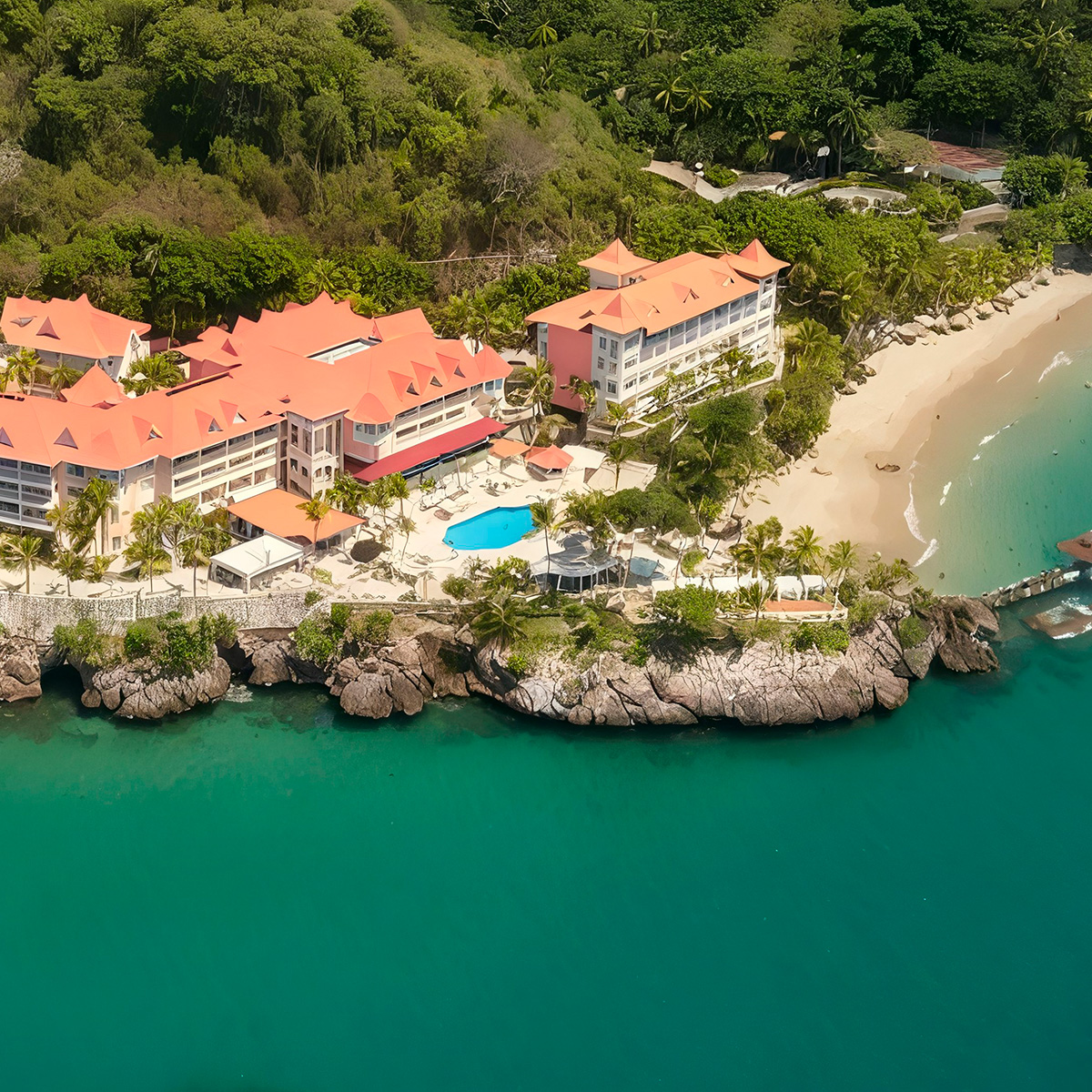 Aerial view of the Bahia Principe Grand Samana, a beachfront resort featuring red roofs nestled amidst lush greenery, with a swimming pool and a sandy beach next to turquoise waters.