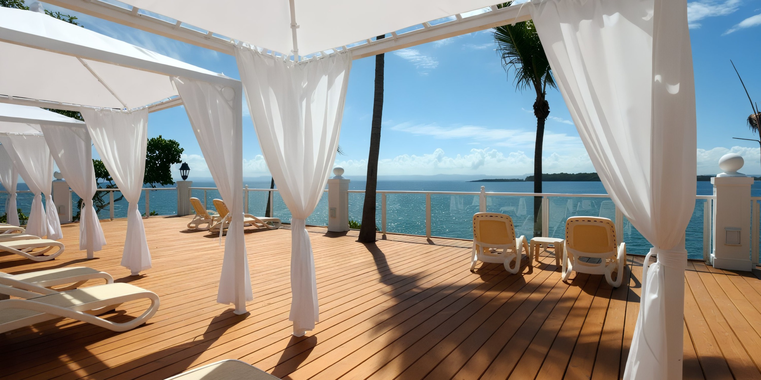 A sunlit deck at the Bahia Principe Grand Samana features white cabanas, lounge chairs, and palm trees overlooking a calm ocean.