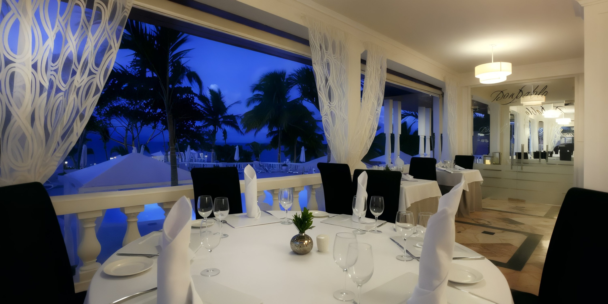 Experience an elegant dining room at the Bahia Principe Grand Samana, featuring round tables adorned with white tablecloths and expertly folded napkins. Large windows showcase a stunning nighttime view of palm trees outside.
