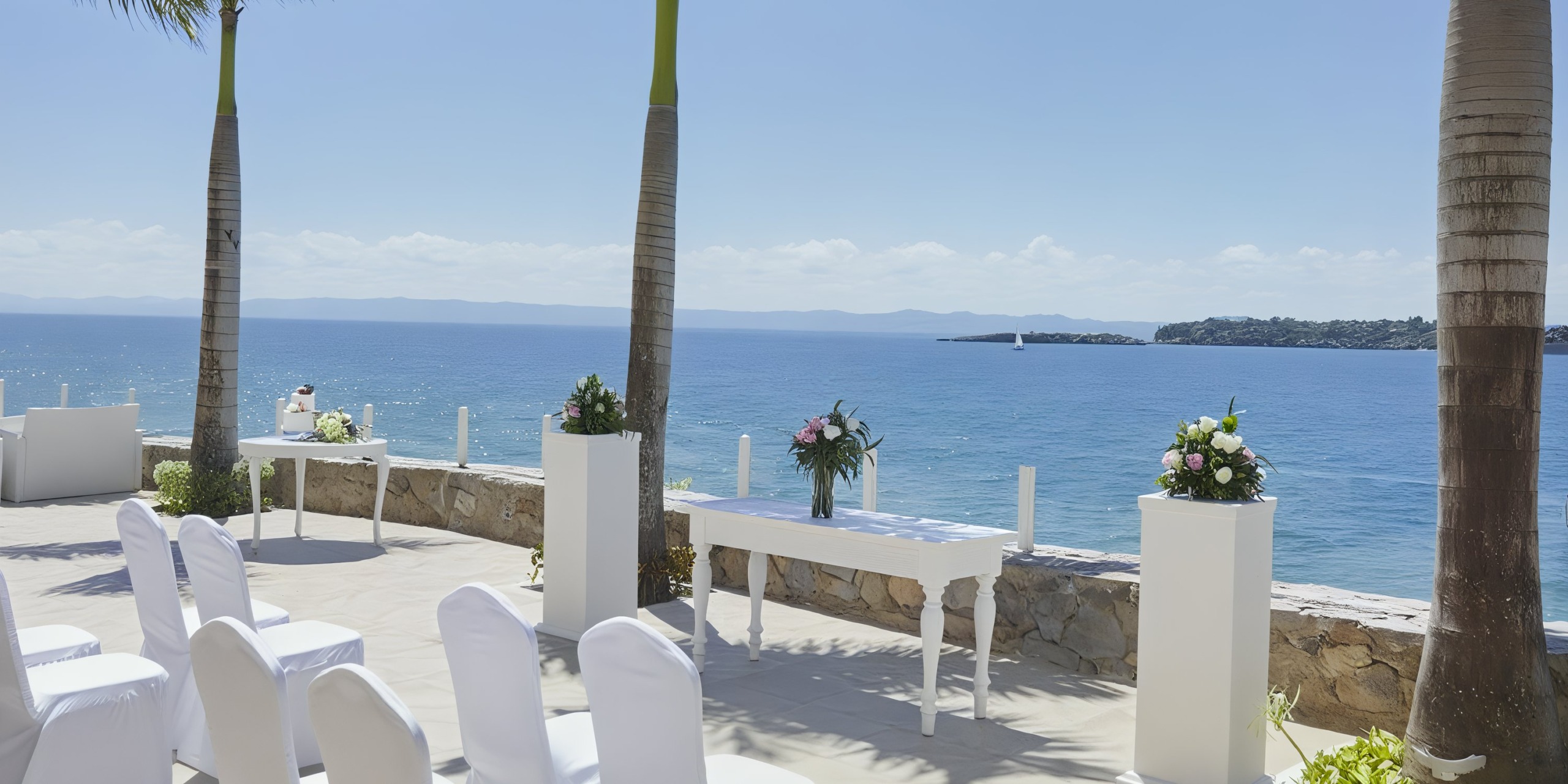Bahia Principe Grand Samana offers a stunning outdoor seaside wedding setup featuring white chairs and tables, exquisite floral arrangements, and palm trees with breathtaking ocean views.