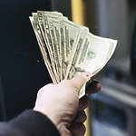 A hand holding a fan of U.S. dollar bills in various denominations.