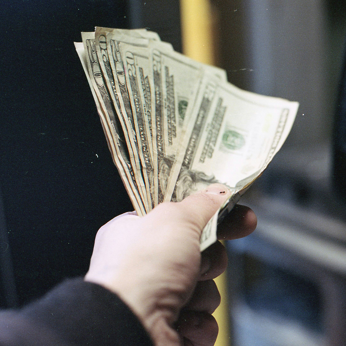 A hand holding a fan of U.S. dollar bills in various denominations.