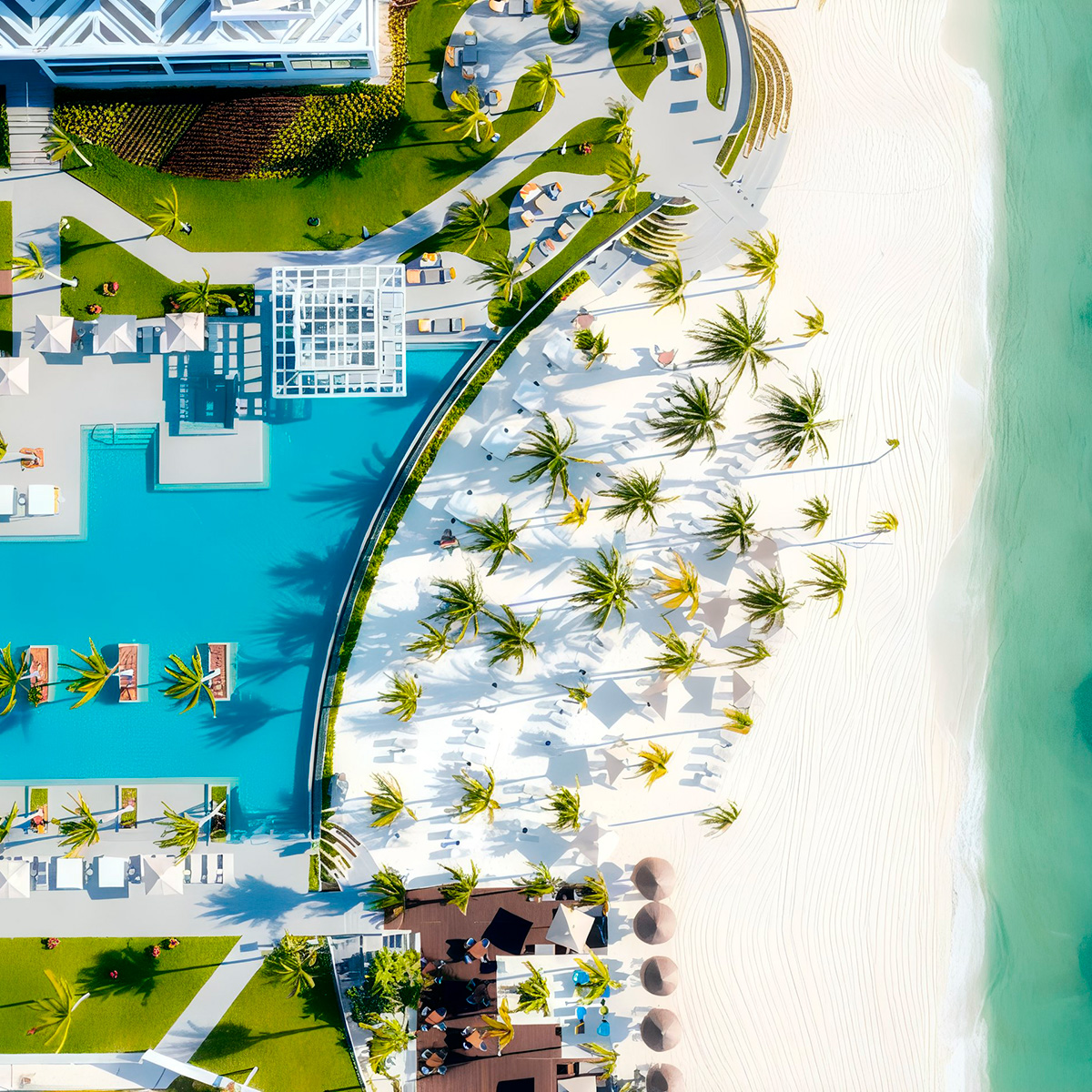 Aerial view of Garza Blanca Cancun, a beachfront resort featuring a pool, surrounded by palm trees and sun loungers on a pristine white sandy beach next to clear turquoise waters.