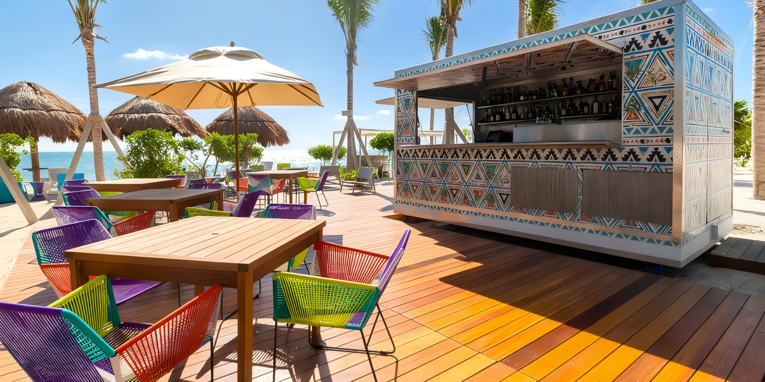 The Garza Blanca Cancun features an outdoor beach bar with vibrant chairs and tables set on a wooden deck, shaded by umbrellas. The bar is adorned with geometric patterns, and palm trees are visible in the background.