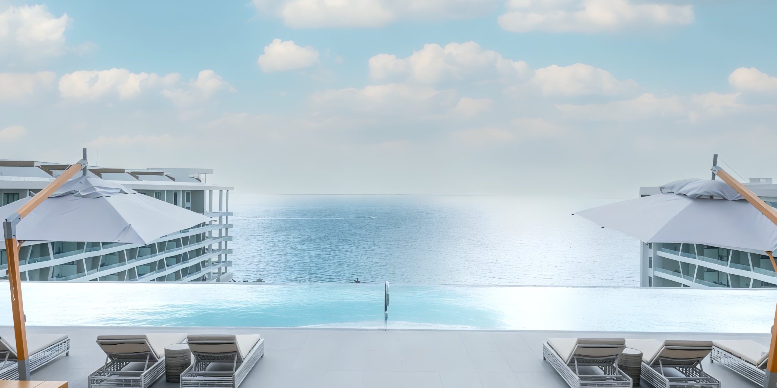 The infinity pool at Garza Blanca Cancun offers breathtaking ocean views, surrounded by comfortable lounge chairs and umbrellas, with buildings on either side under a partly cloudy sky.