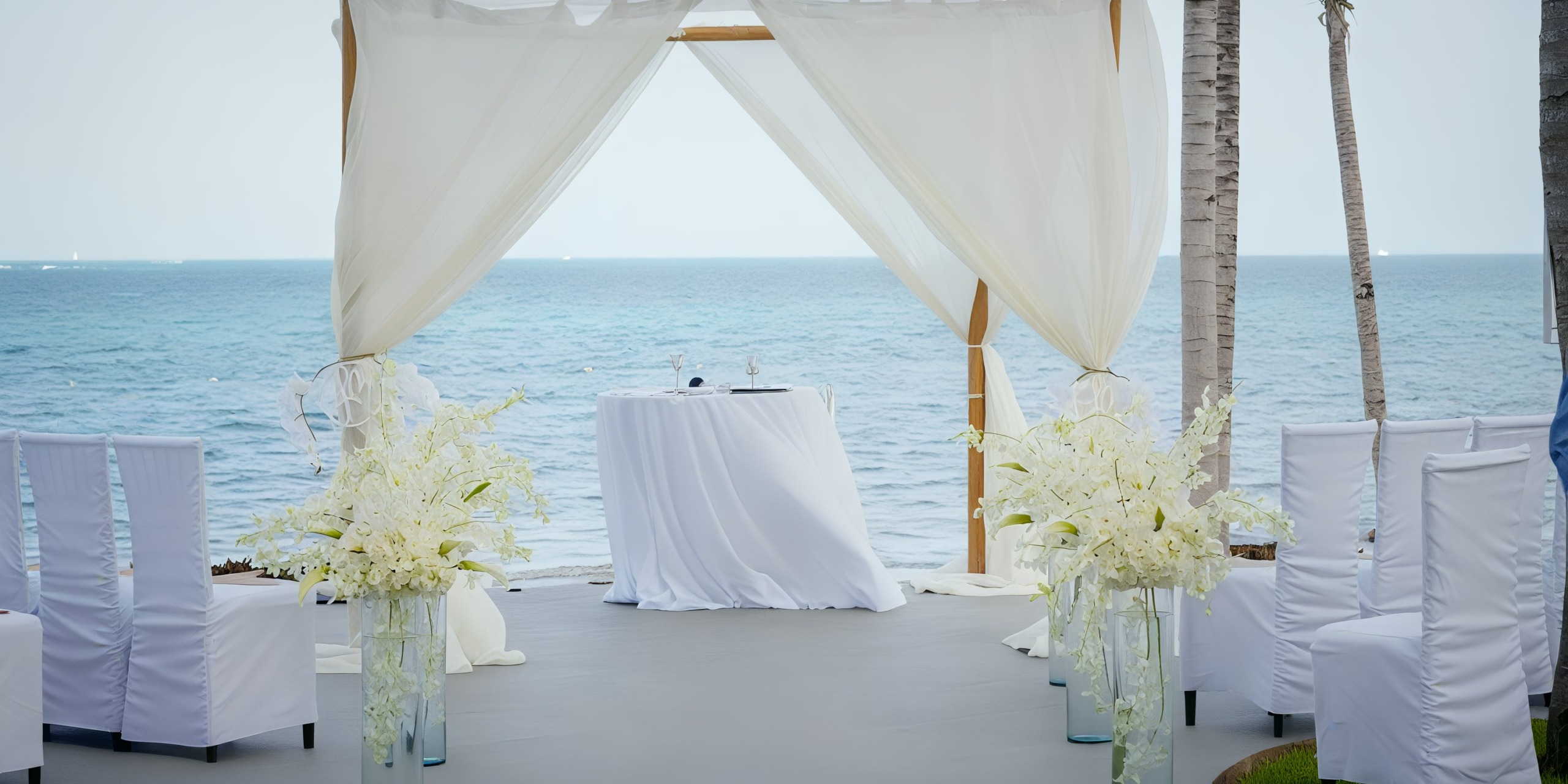 Garza Blanca Cancun offers a wedding altar setup by the sea, featuring white drapes, chairs, and exquisite floral arrangements.