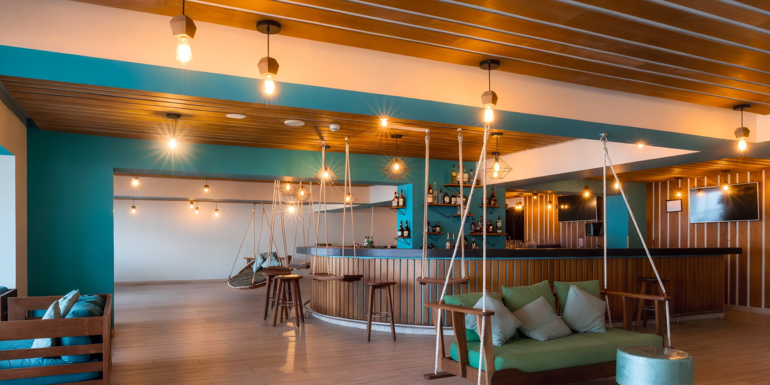 Experience the Hilton Vallarta Riviera All-Inclusive Resort, featuring a modern lounge adorned with a wooden ceiling, teal accents, a stylish bar complete with stools, inviting hanging chairs, and plush cushioned seating. The warm lighting enhances the cozy ambiance throughout.