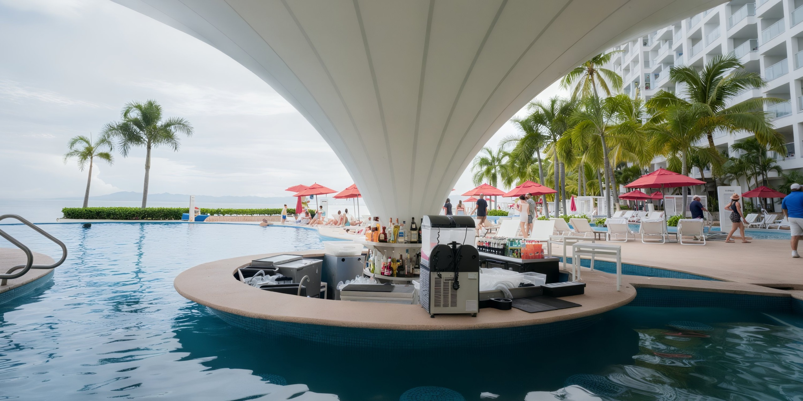 Set against a backdrop of water and palm trees, the poolside bar at the Hilton Vallarta Riviera All-Inclusive Resort boasts a canopy, complemented by red umbrellas and lounge chairs.