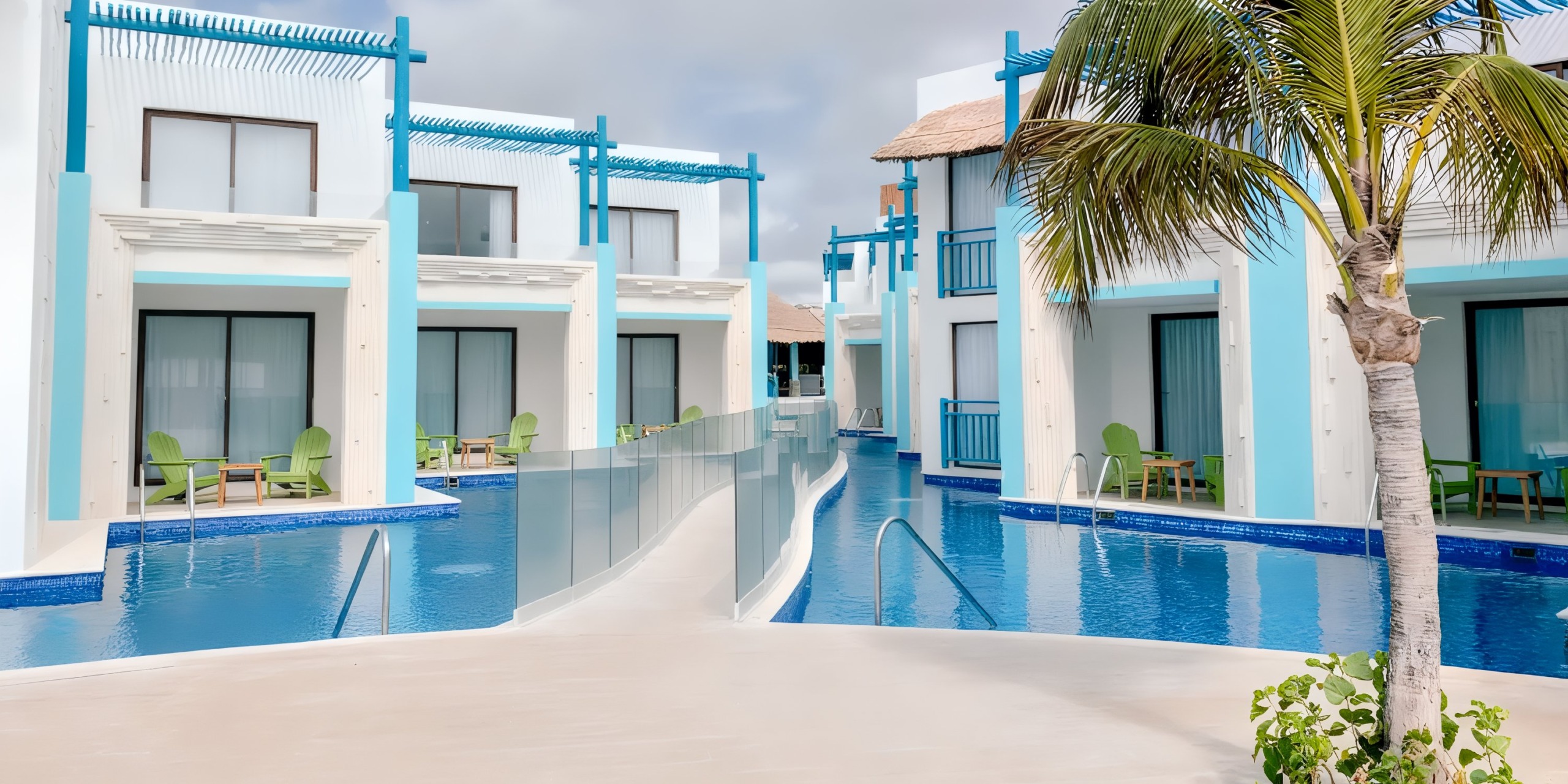 The Margaritaville Island Reserve Resort Riviera Cancun features modern blue and white buildings surrounding a pool, enhanced by palm trees and green chairs to create a tropical atmosphere.