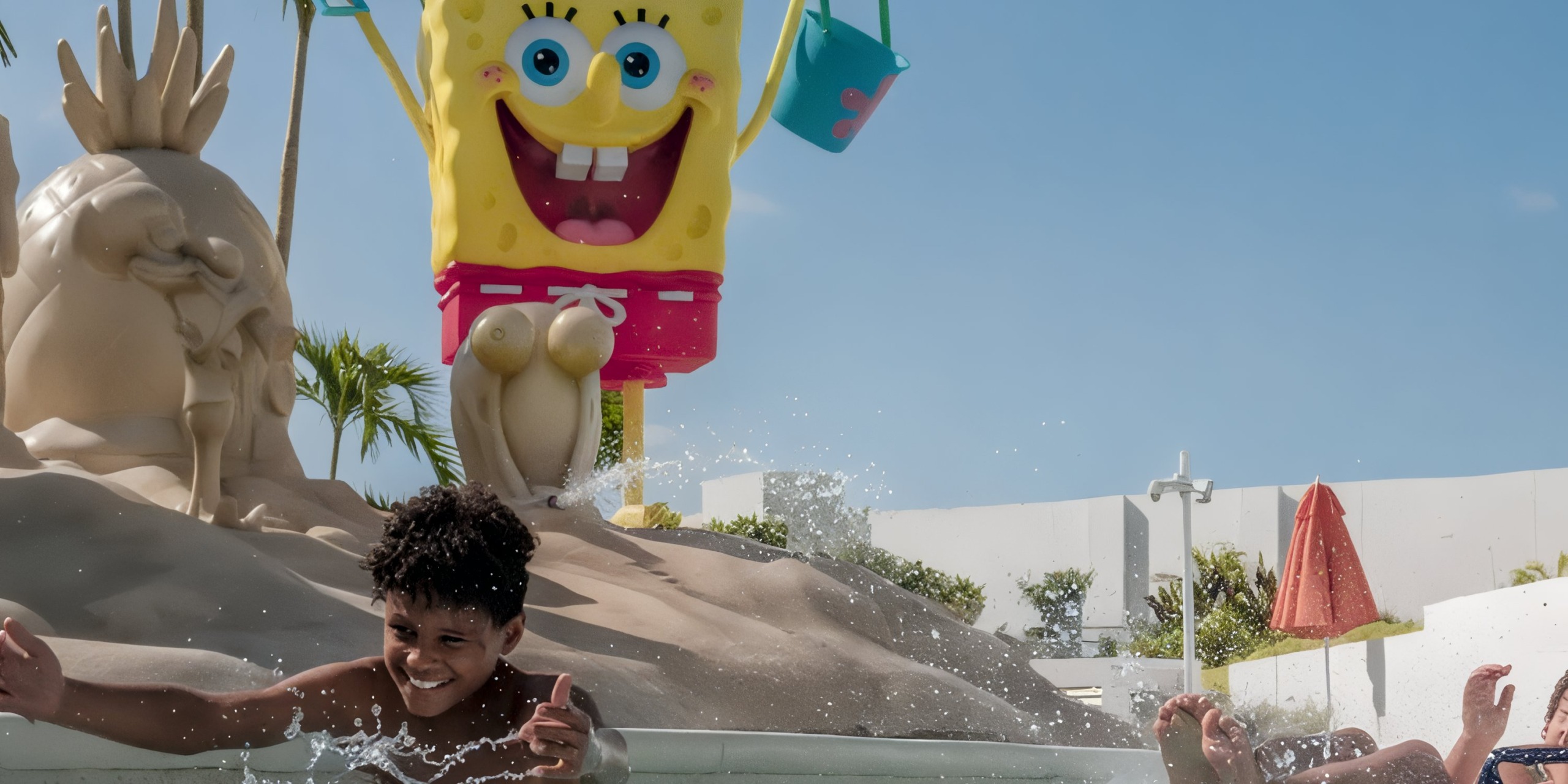 Two children play in a pool near a large statue of SpongeBob SquarePants holding a bucket at the Nickelodeon Hotels & Resorts Riviera Maya.
