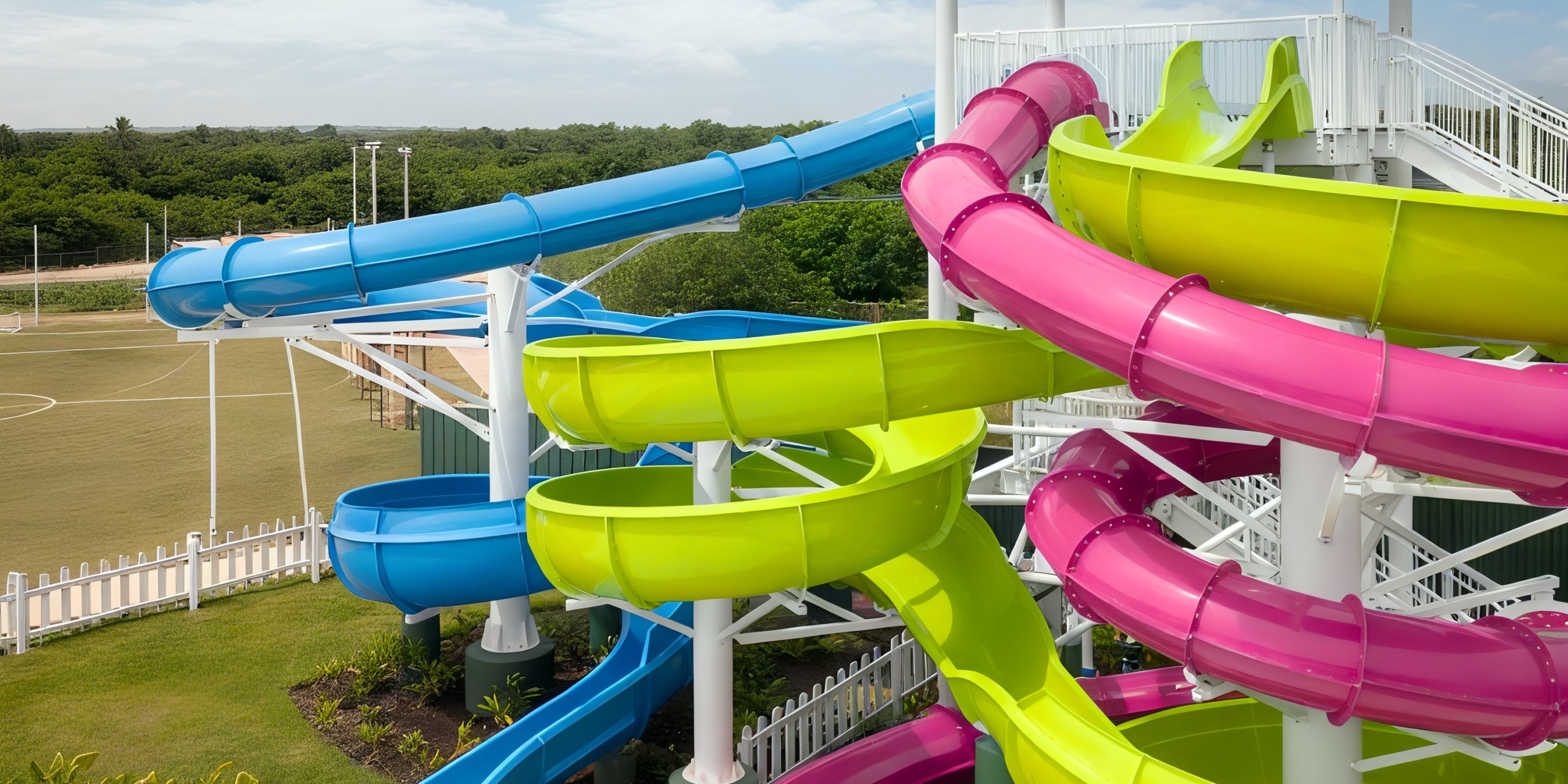 Experience the vibrant water slides with twists and turns, featuring blue, green, and pink slides at Nickelodeon Hotels & Resorts Riviera Maya, all set in an outdoor area surrounded by trees.