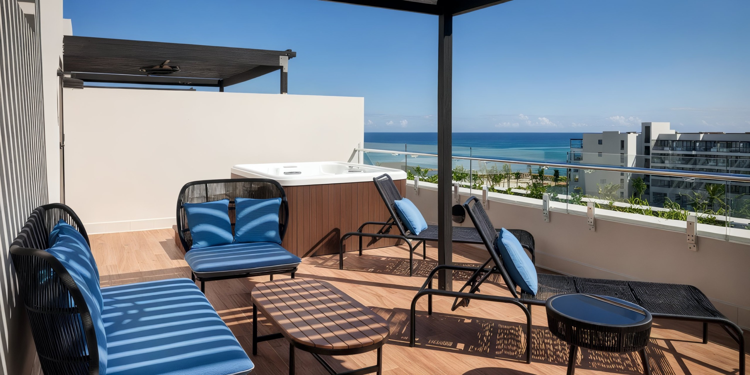 Experience the Ocean Eden Bay rooftop terrace, featuring a hot tub, blue cushioned loungers, chairs, and a small table with breathtaking ocean views on a clear day.