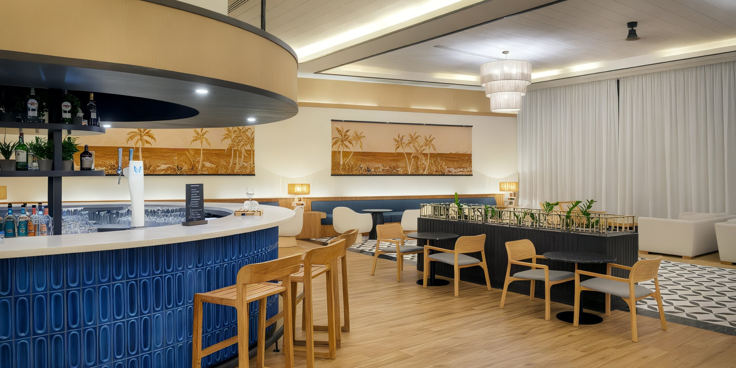 Experience the Ocean Eden Bay, a modern lounge area featuring a stylish curved bar with wooden stools and palm-themed artwork. The space is designed with a blend of seating options and contemporary lighting, highlighting the light wood floor and neutral decor.
