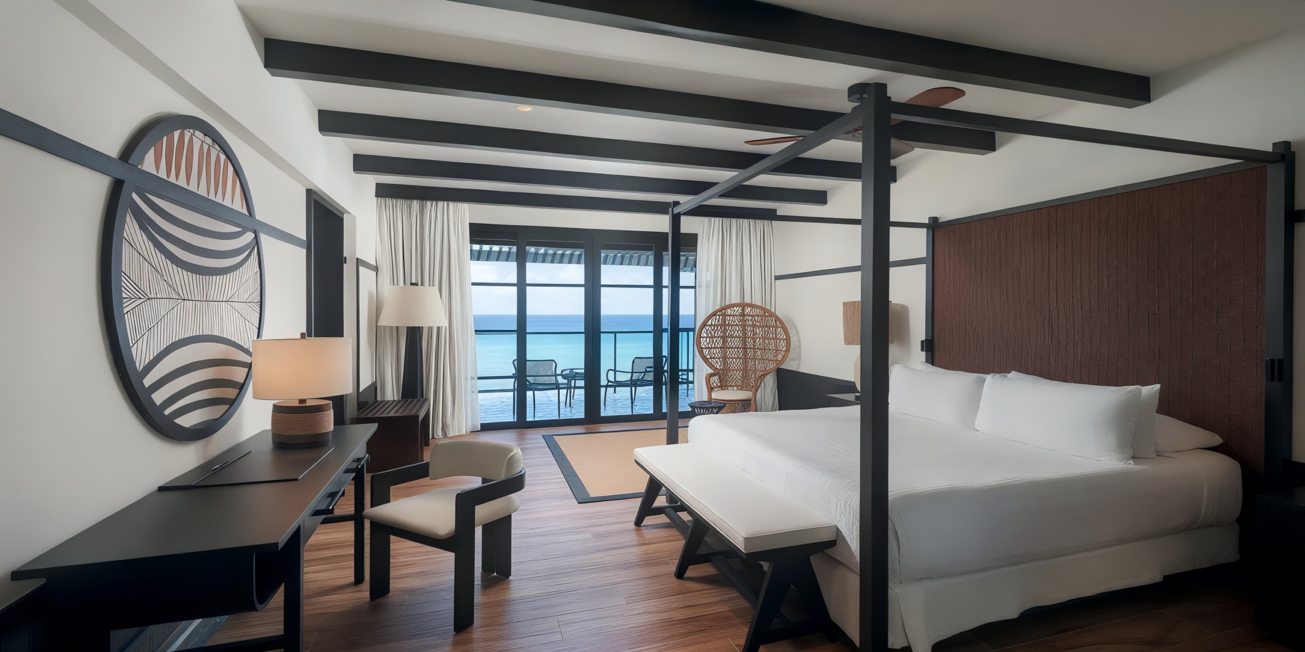 Experience a luxurious stay at Ocean Eden Bay, featuring a well-appointed room with a canopy bed, desk, chair, and balcony offering stunning ocean views. The serene atmosphere is enhanced by neutral tones and modern decor.