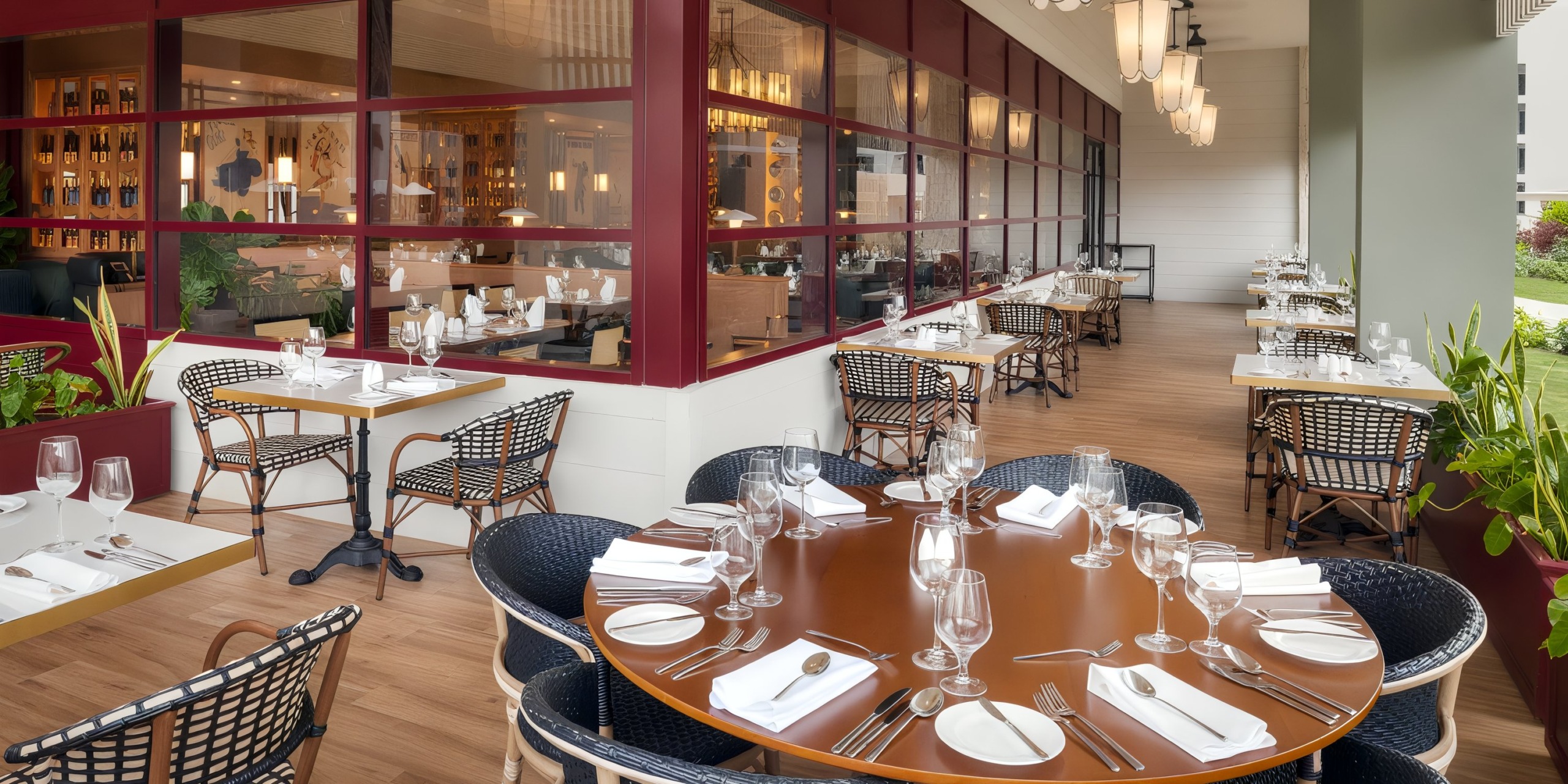 Ocean Eden Bay features an outdoor patio equipped with wooden dining tables, lush plant surroundings, and a scenic view of the indoor dining area through expansive glass windows.