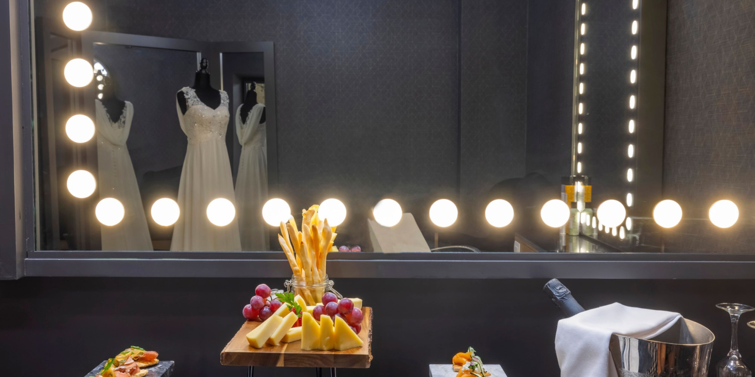 In a luxurious suite at Planet Hollywood Adult Scene All Suites Cancun, the mirrored table showcases an array of fruit, cheese, and snacks. The enchanting reflection of a wedding dress on a mannequin captivates the room's ambiance.