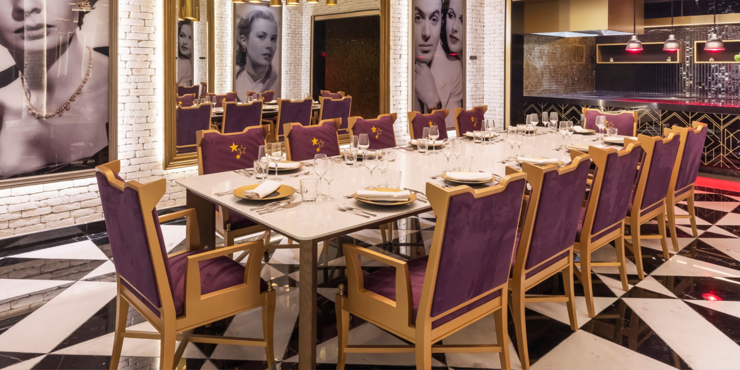 The dining area in the Planet Hollywood Adult Scene All Suites Cancun boasts a sophisticated large table set for a meal, encircled by plush purple chairs. The walls are adorned with striking black and white portraits, while the floor showcases an eye-catching black and white geometric pattern.