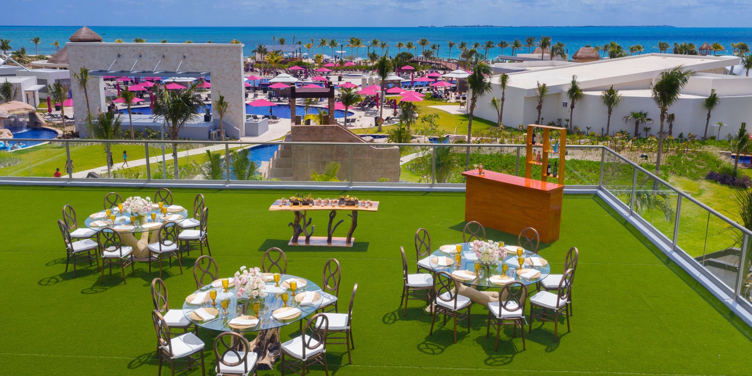A scenic view of the Planet Hollywood Adult Scene All Suites Cancun rooftop event setup with decorated tables overlooking a beach and vibrant landscape.