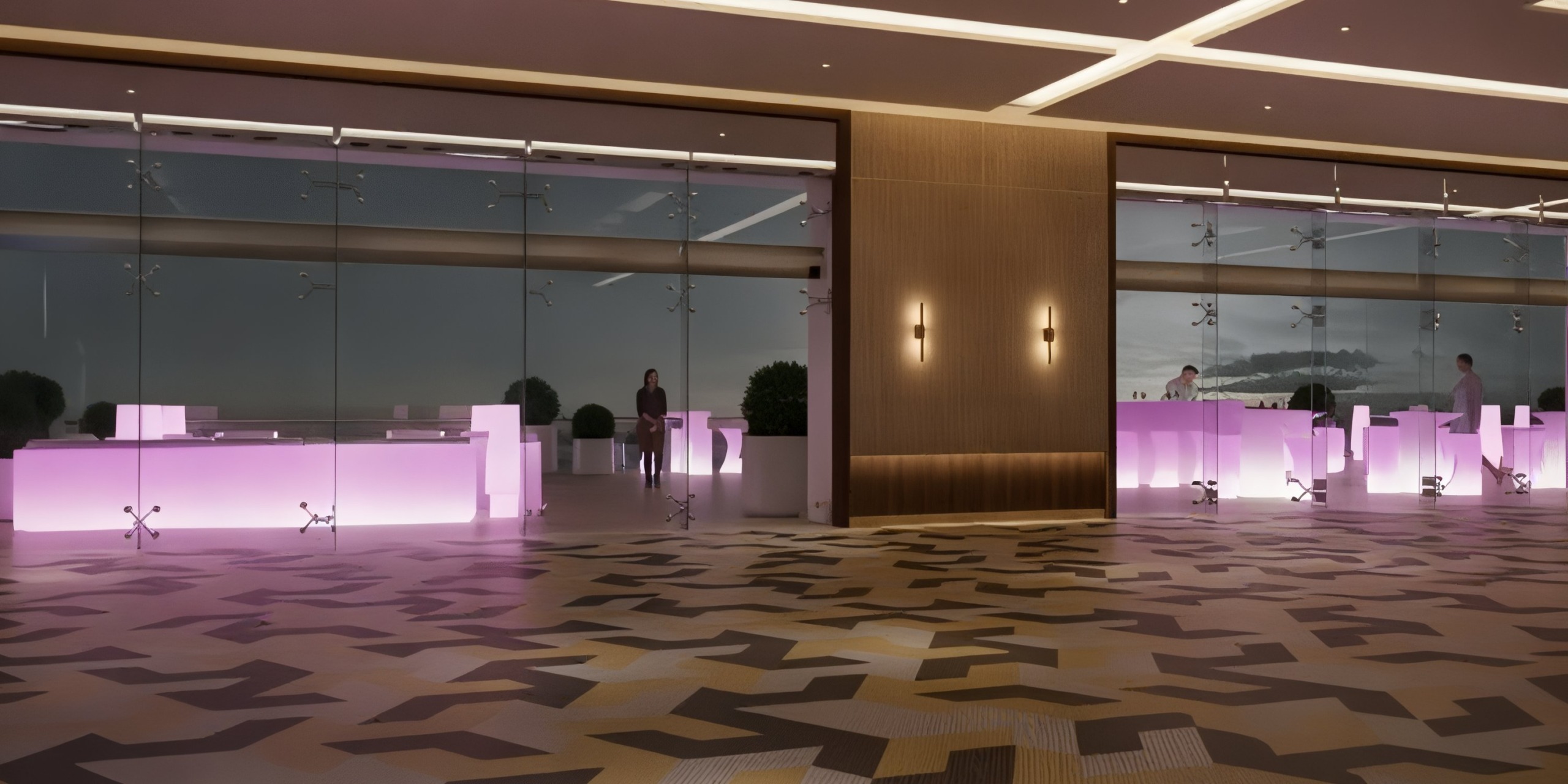 The Princess Grand Jamaica features a contemporary empty lobby with a floor adorned in geometric patterns, illuminated rectangular reception desks, and a backdrop of glass walls.