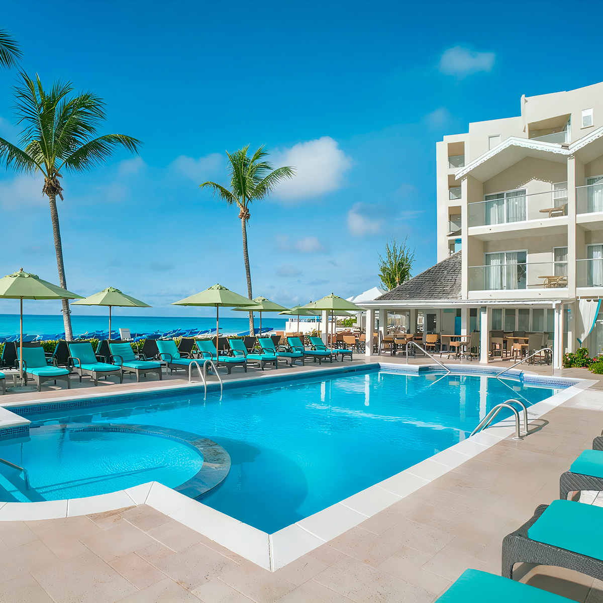 The pool area at Sea Breeze Beach House by Ocean Hotels features lounge chairs and umbrellas, set amidst palm trees, with a stunning ocean view.