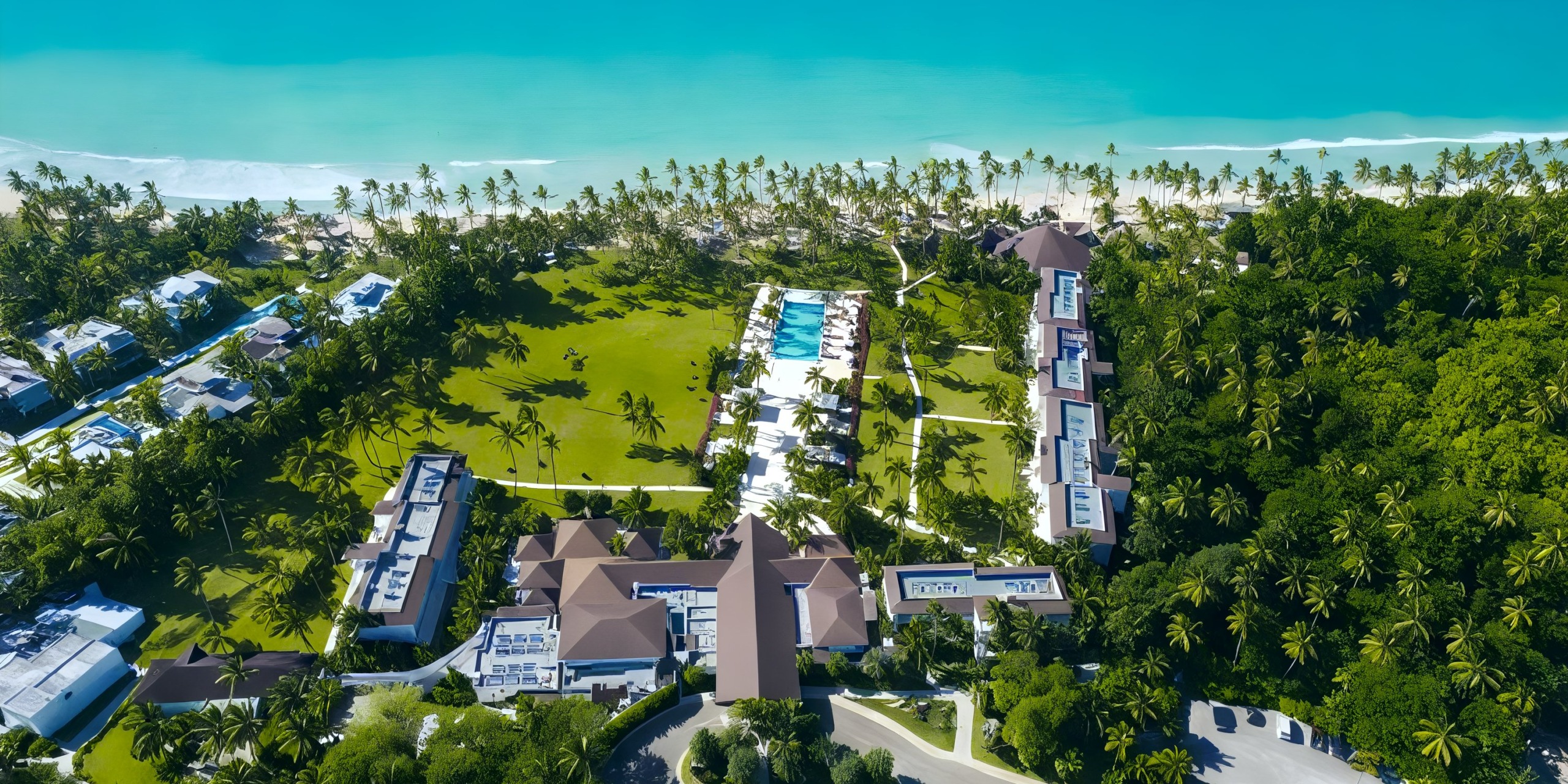 Aerial view of Viva V Samana by Wyndham, a beachfront resort featuring multiple buildings, a large pool, and palm trees set against the backdrop of turquoise ocean water.