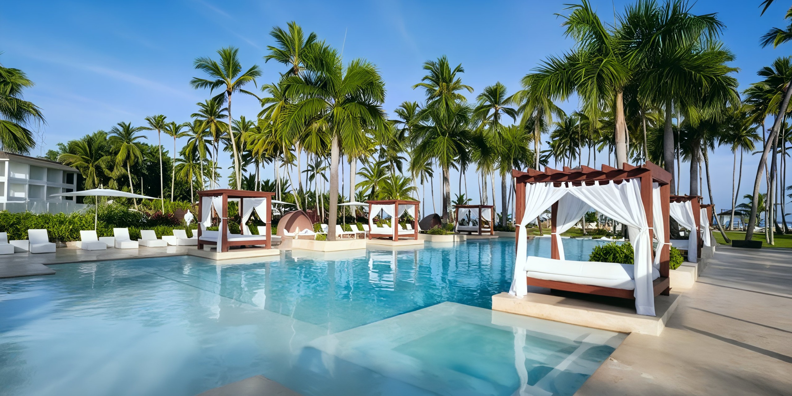 The pool area at Viva V Samana by Wyndham offers a luxurious experience with lounging cabanas and surrounding palm trees under a clear blue sky.