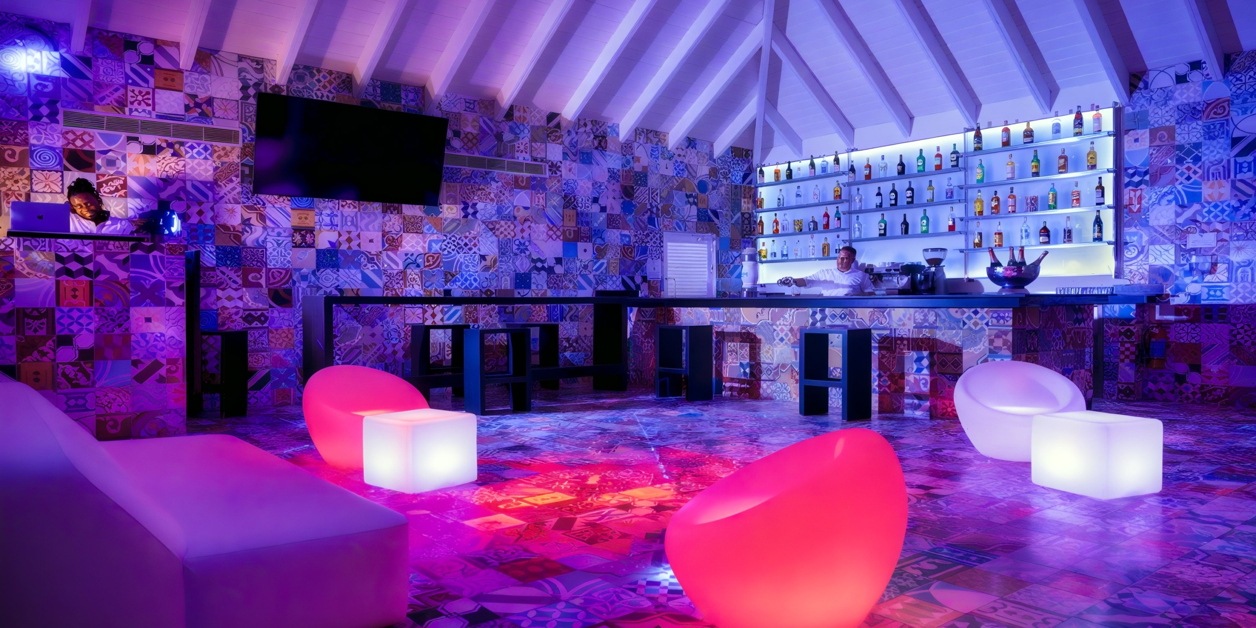 The Viva V Samana by Wyndham boasts a vibrant bar with a contemporary design, highlighted by mosaic tiles, illuminated furniture, and a fully stocked bar with backlit shelves.